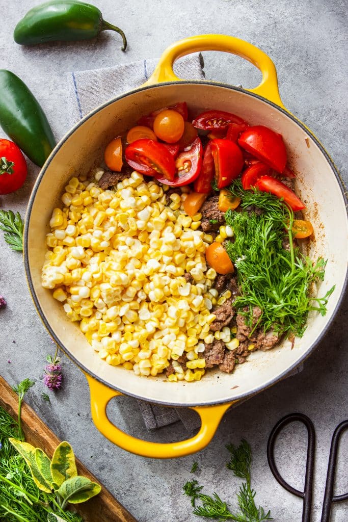 ground beef in skillet with corn, tomatoes and fresh herbs.