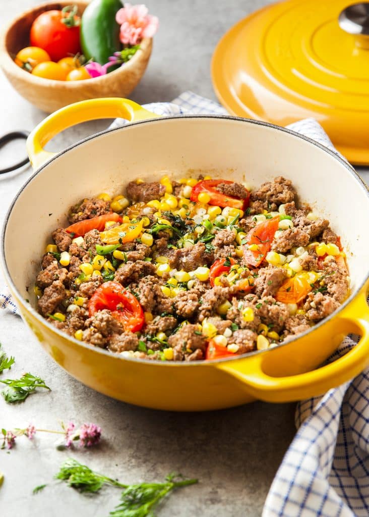 ground beef, corn and tomato skillet, garnished with fresh herbs. Herbs and flowers on the table, a table cloth.