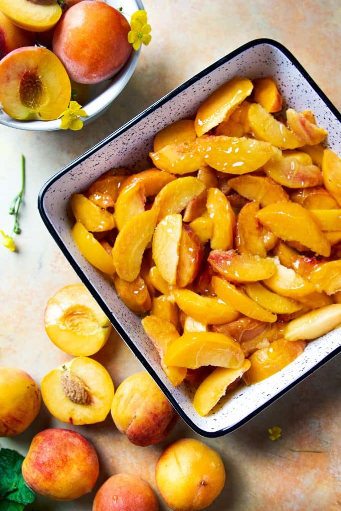 baking dish with peach slices. Extra peaches on the table.