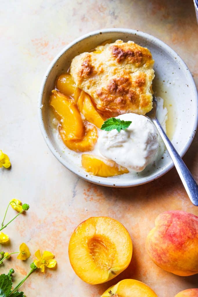 A serving of peach cobbler with vanilla ice cream. Fresh mint on top