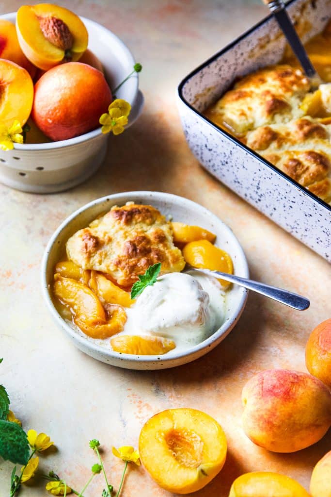 a serving of peach cobbler on a small plate with vanilla ice cream. 