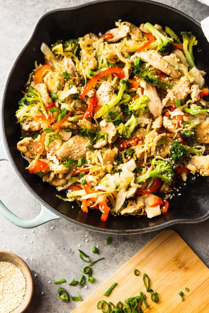 Chicken stir fry recipe in a skillet. A few herbs on the table.
