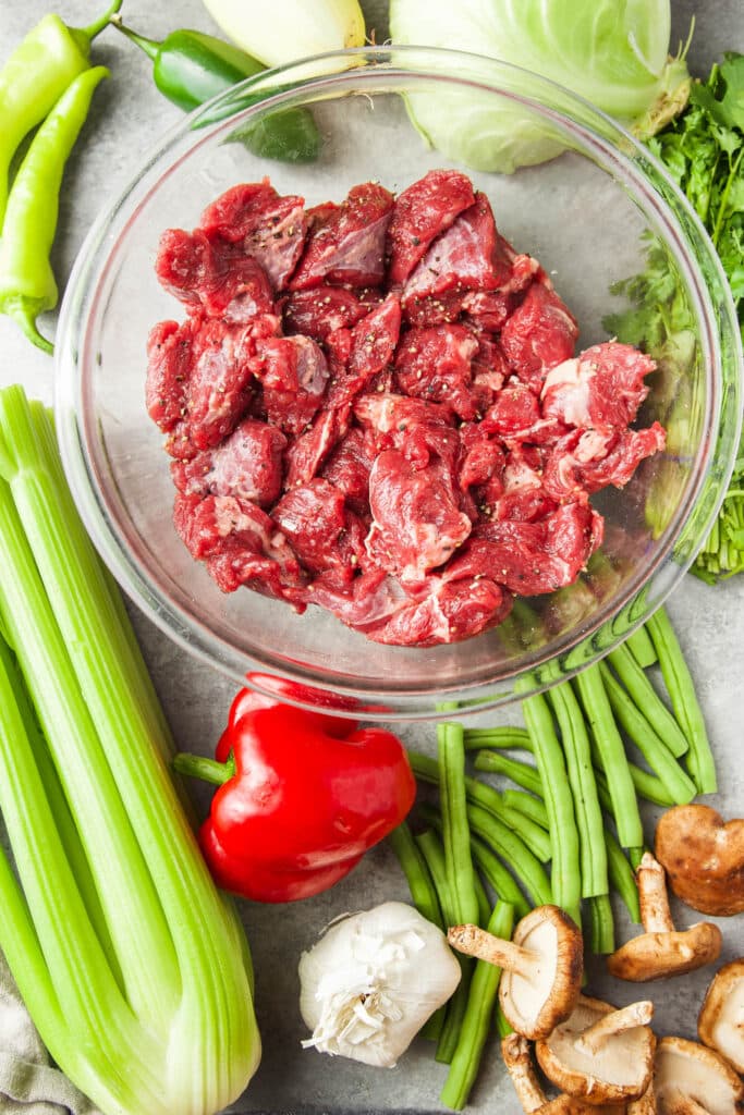 Ingredients for low carb keto beef stew. Meat in a glass bowl. Veggies on the table. 