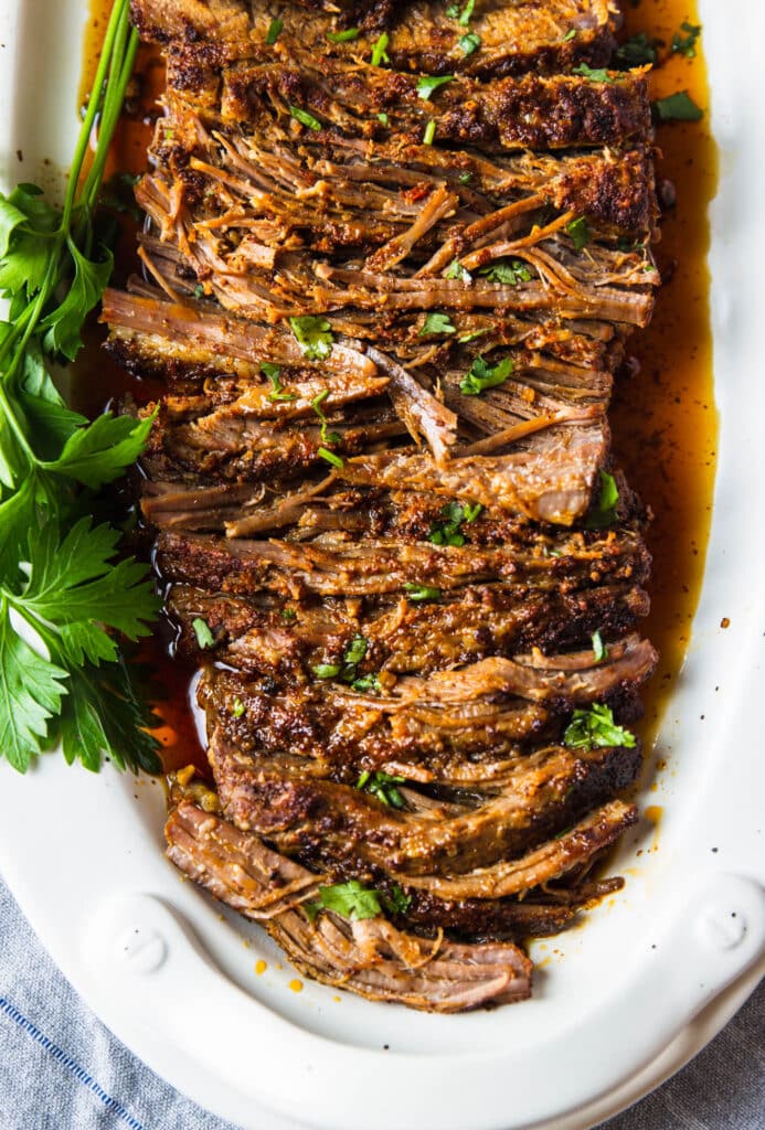 Slow cooked oven roasted beef brisket in a serving platter with fresh herbs. 