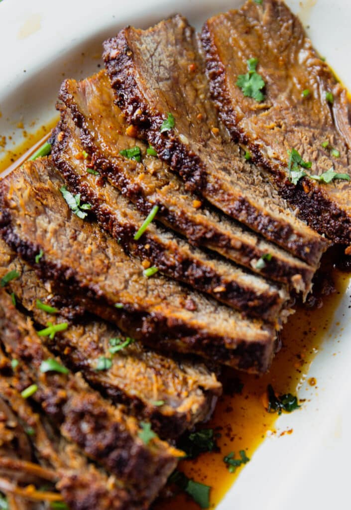 Close up image of sliced beef brisket, garnished with fresh herbs.