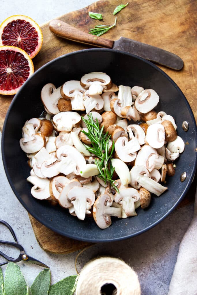 Baby Bella mushrooms sliced in skillet with garlic and rosemary 