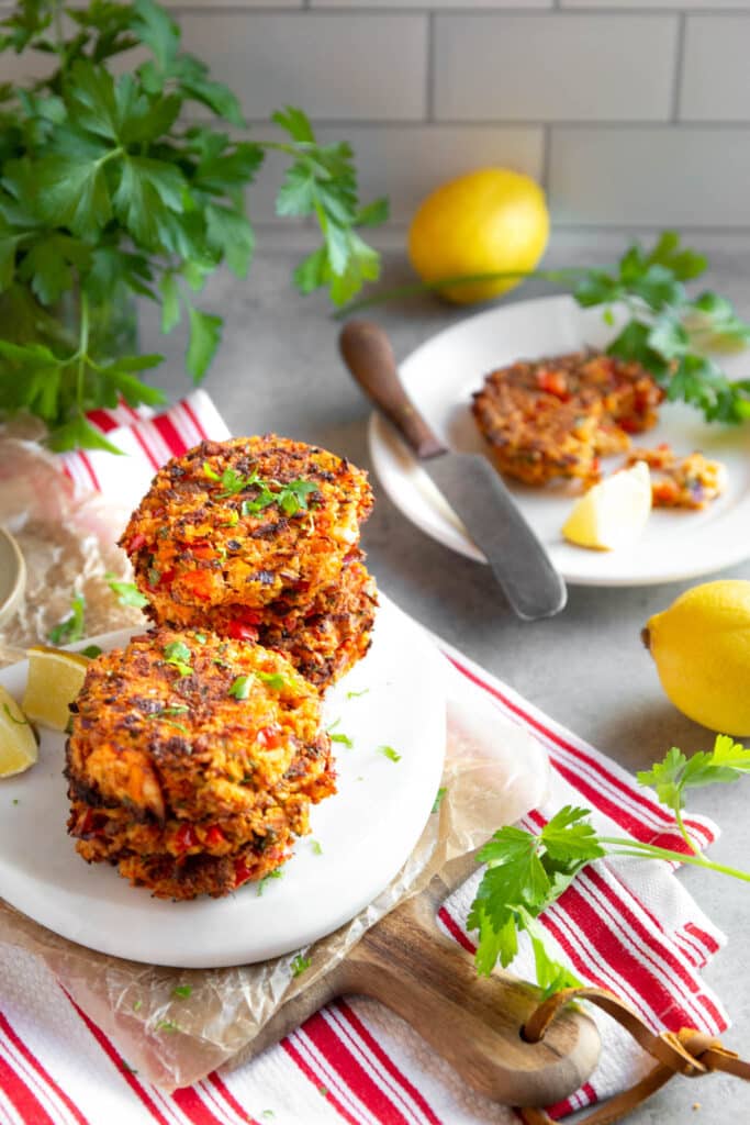 gluten-free salmon cakes on a white serving board, sitting on a red kitchen towel. Fresh herbs and lemons on the table. 