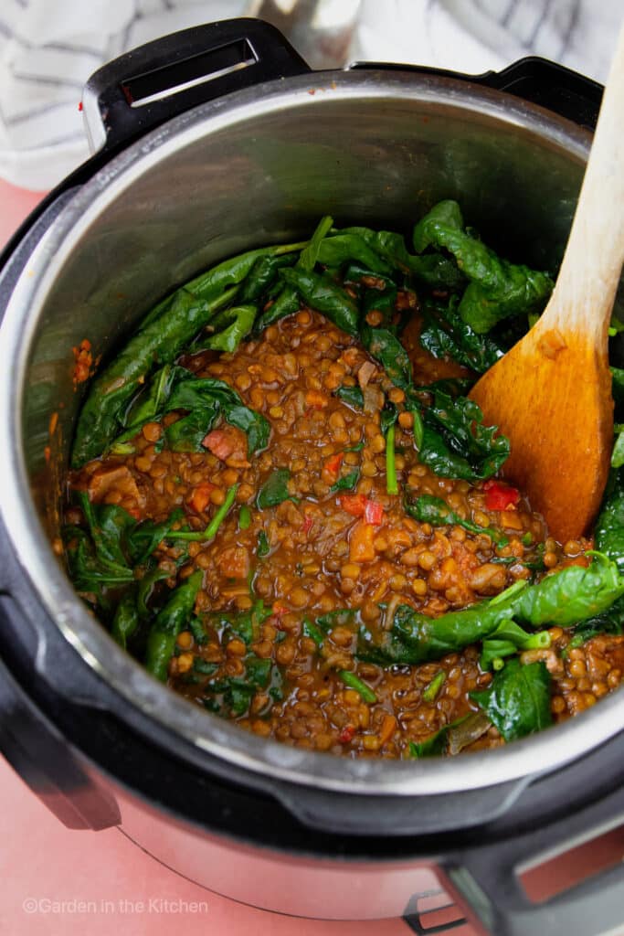 French Green Lentil Soup in a instant pot with fresh spinach and a wooden spoon.