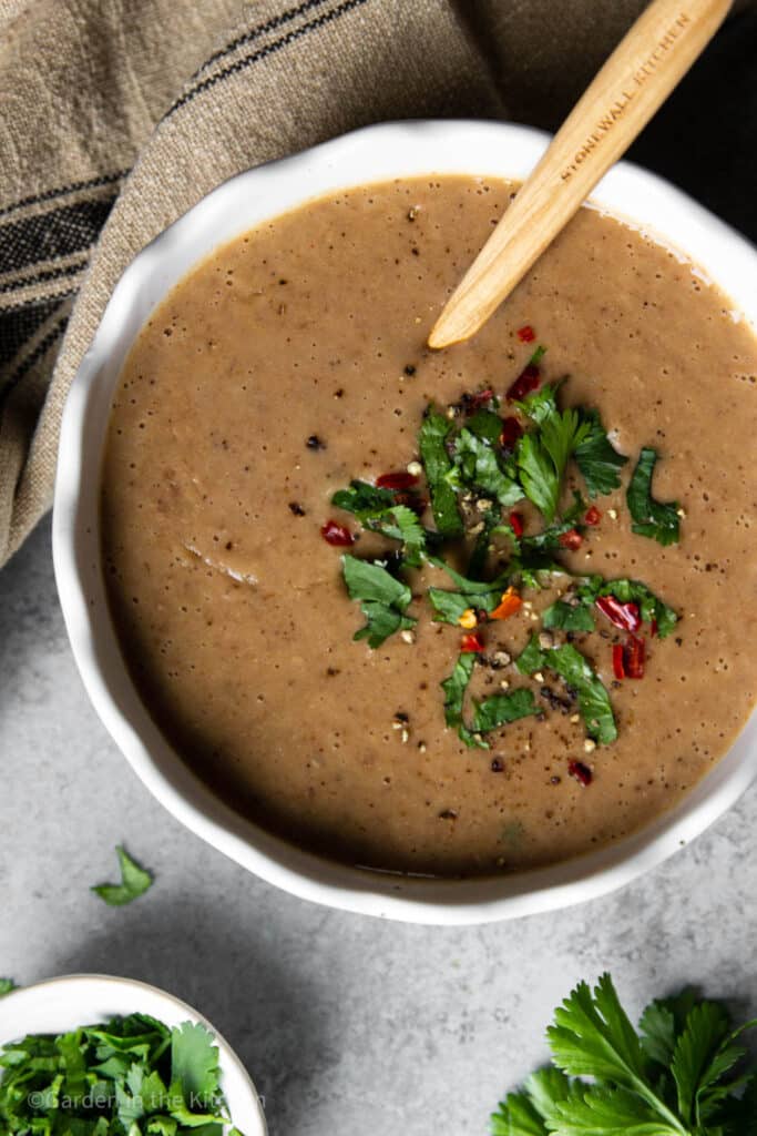 Instant pot Mexican refried beans in a white bowl with a wooden spoon garnished with fresh cilantro and red pepper flakes.