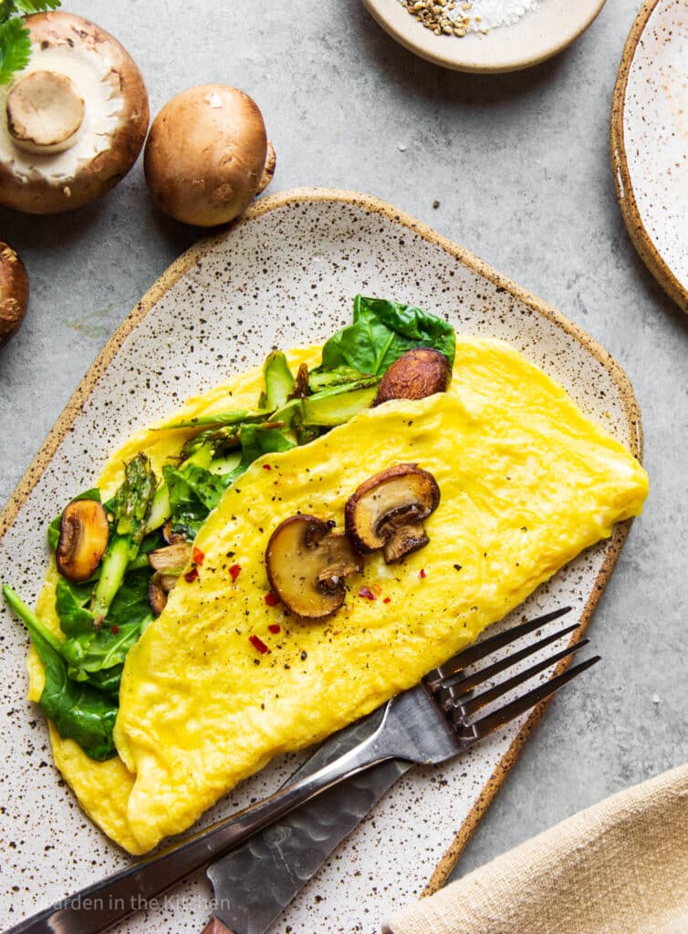 A healthy mushroom, spinach and asparagus egg omelette on a plate with a fork and knife. 