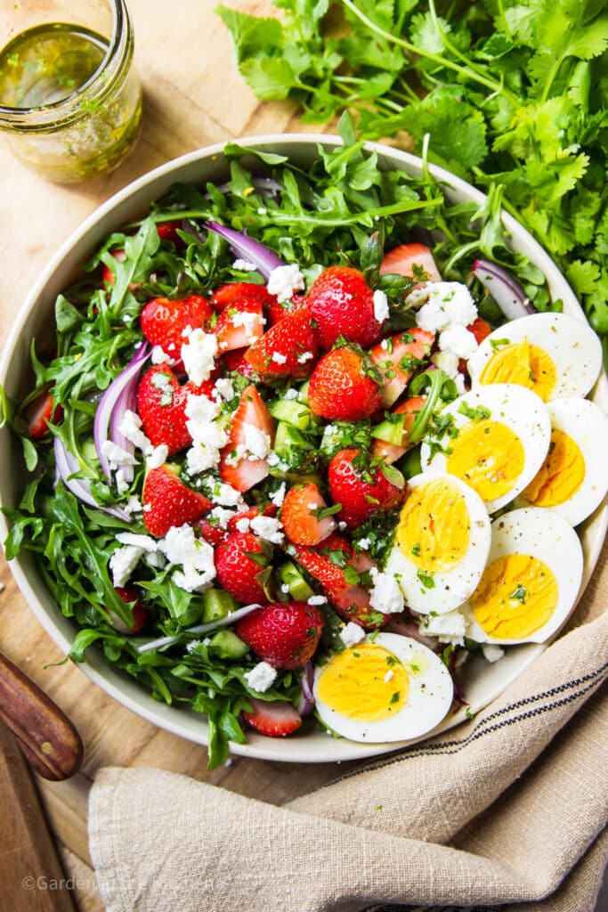 Salad in a bowl with strawberry, arugula, feta, red onions and hard boiled eggs.