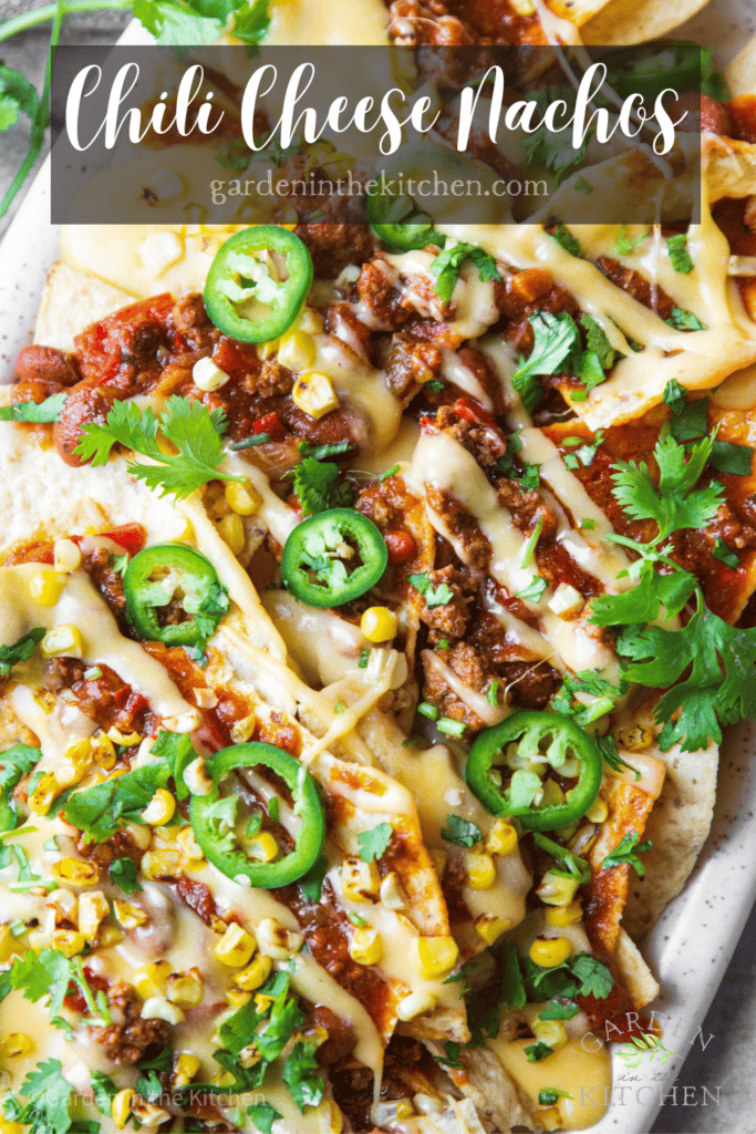 Chili cheese nachos on a platter with jalapeño, corn and cilantro. 