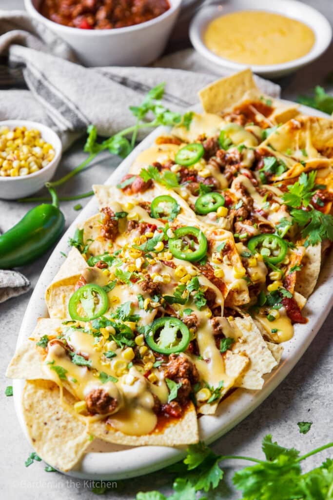 Chili cheese nachos on a platter topped with jalapeño, corn and cilantro. Fresh ingredients on the table. 