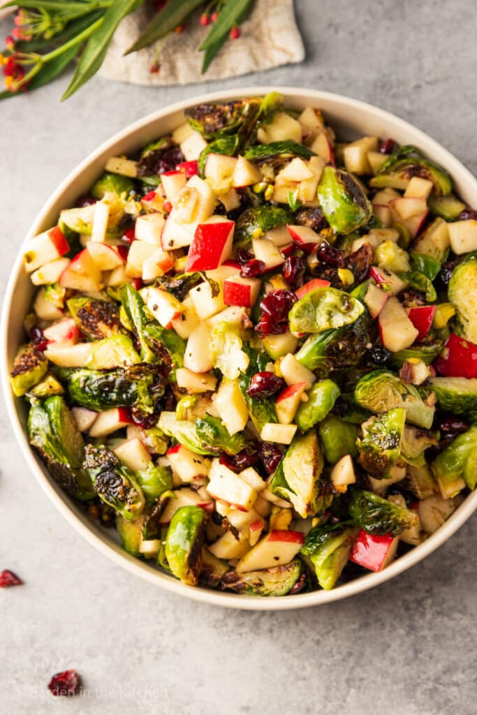 Maple Roasted Brussels Sprouts and Apple Salad filled with vegetables, fruit, and nuts, and drizzled in a maple balsamic vinaigrette. Served on a round plate with fresh herbs.