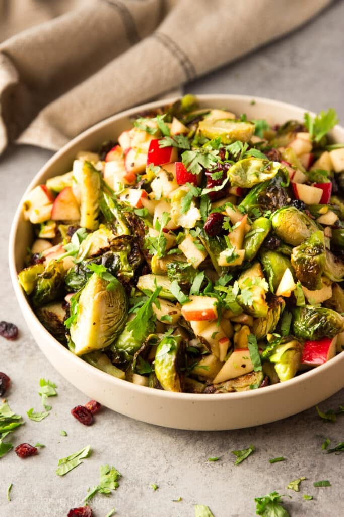 Maple Balsamic Roasted Brussels Sprouts and Apple Salad filled with vegetables, fruit, and nuts, and drizzled in a maple balsamic vinaigrette. Served on a round plate with fresh herbs.
