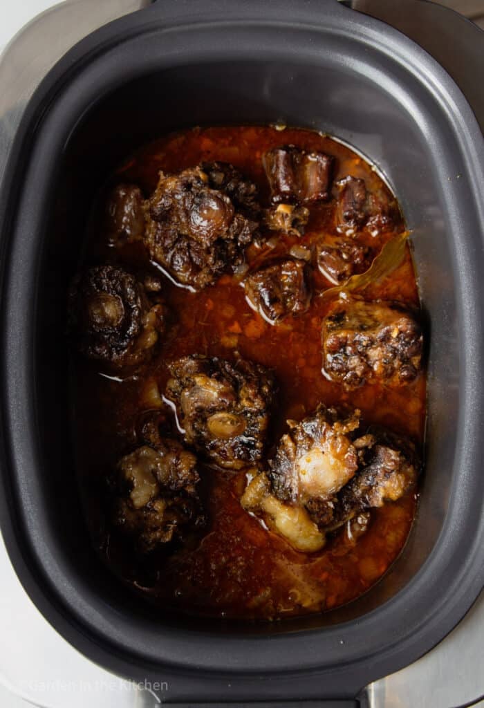 Slow cooker oxtail recipe inside slow cooker with broth. 