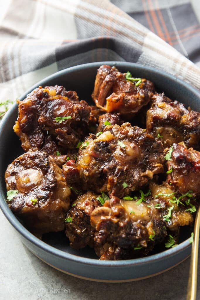Jamaican oxtail recipe in slow cooker served in blue round plate with herbs as garnishing. 