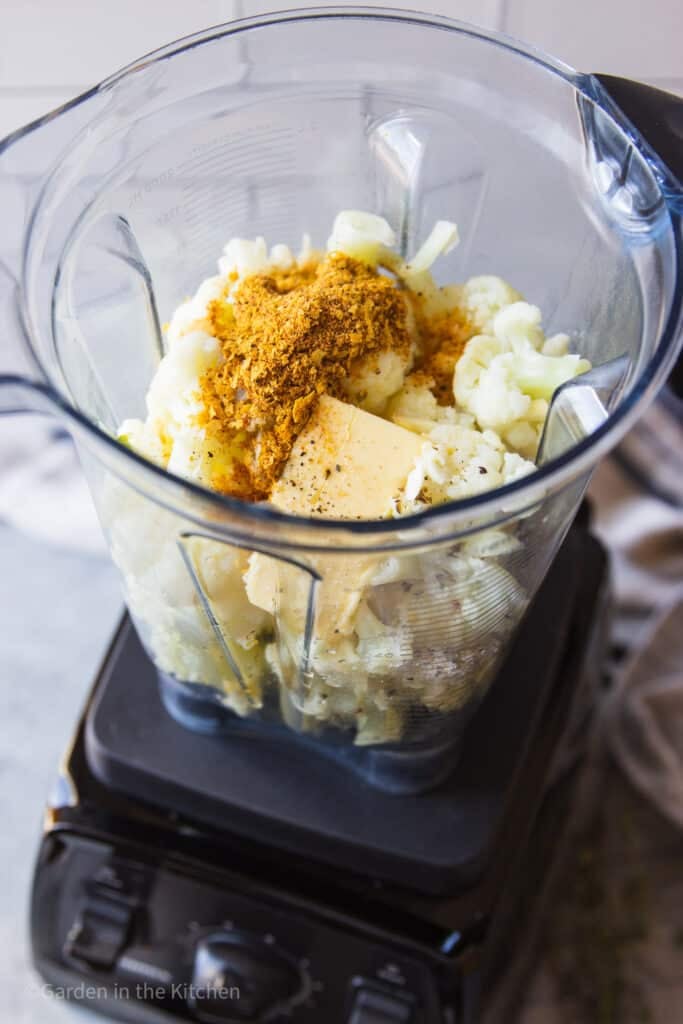Cauliflower florets, butter, seasoning and nutritional yeast inside of a blender cup. 