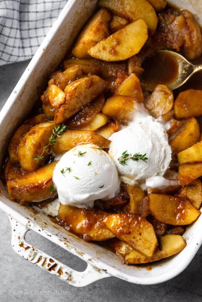 Healthy baked cinnamon apple dessert with two scoops of vanilla ice cream and fresh thyme on top. 