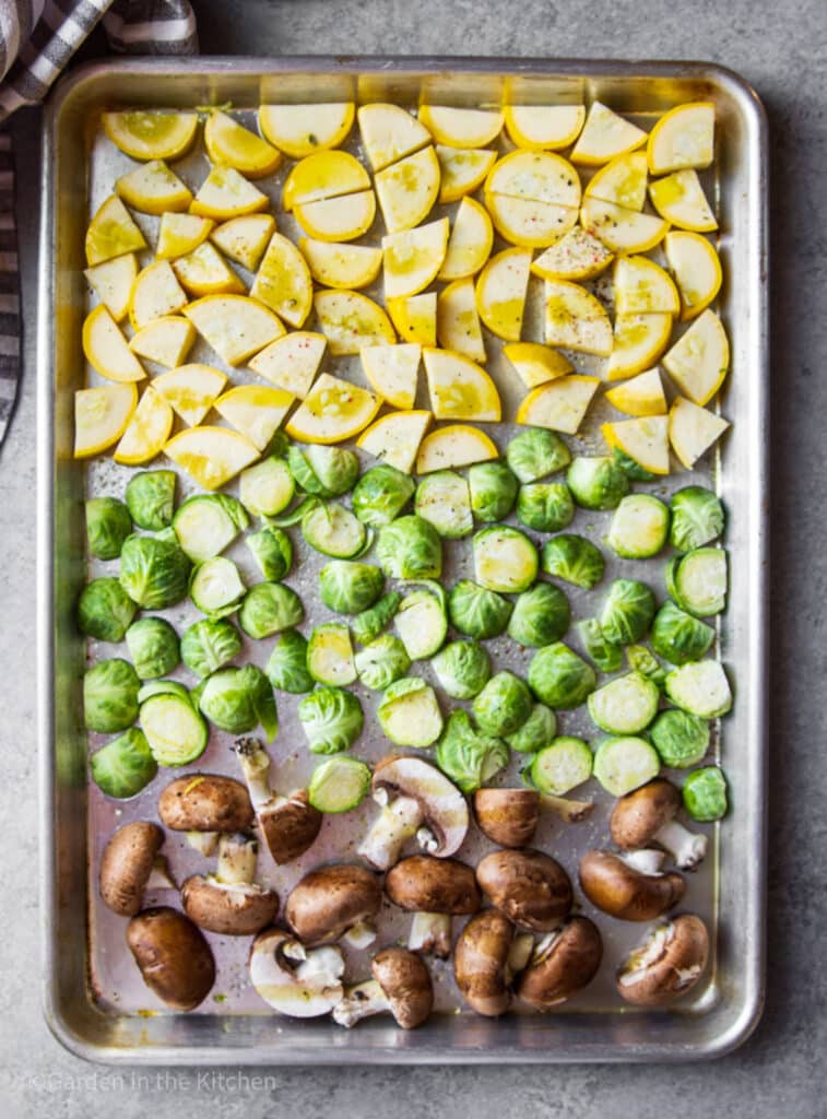 Yellow squash, Brussel sprouts and mushrooms on a sheet pan, seasoned and ready to cook.
