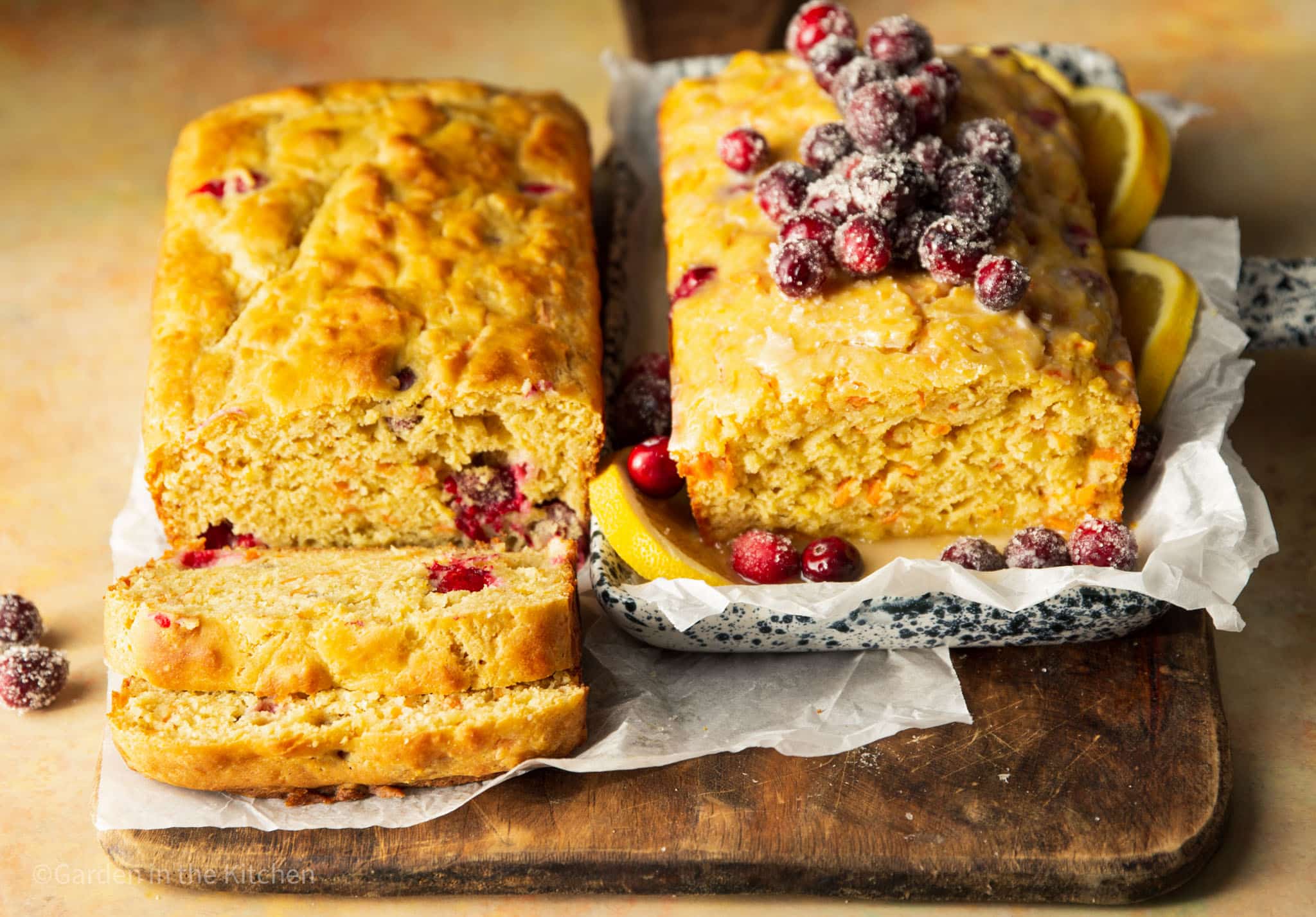 two cranberry orange carrot cakes next to each other. One being sliced and the other topped with sugared cranberries.