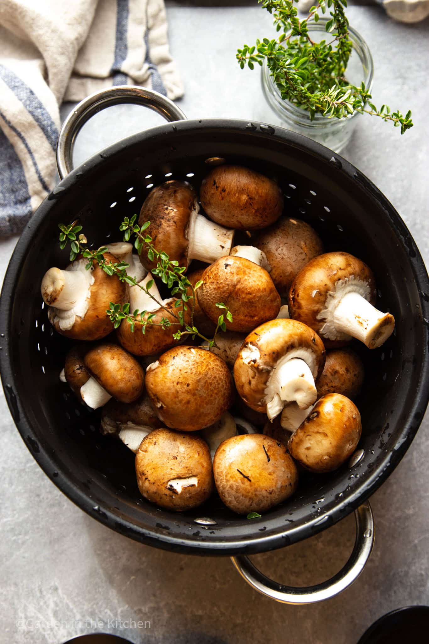 Rinsed mushrooms in a black strainer. A sprig of fresh thyme on top.