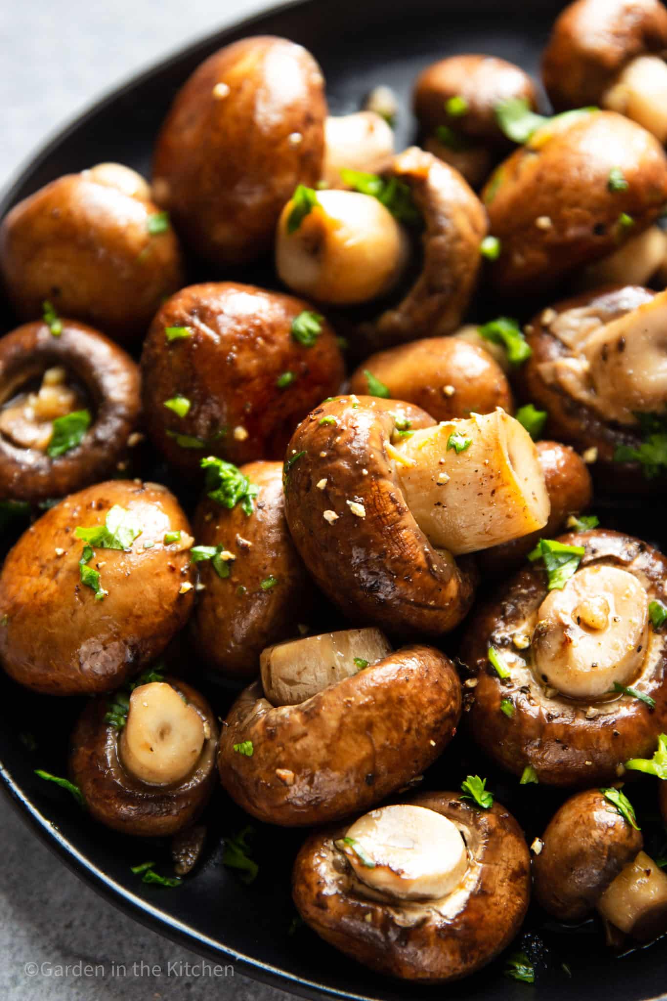 Close up image of cremini mushrooms cooked in garlic butter sauce. Mushrooms are garnished with fresh cilantro.