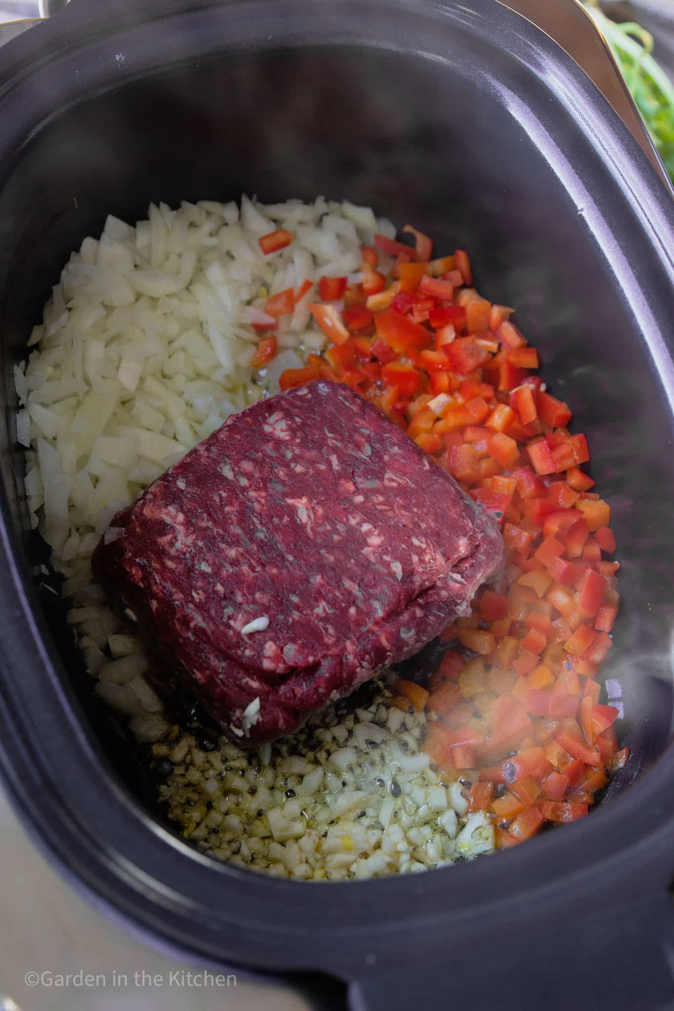 cooking raw ground meat, peppers, onions, and garlic in a slow cooker.