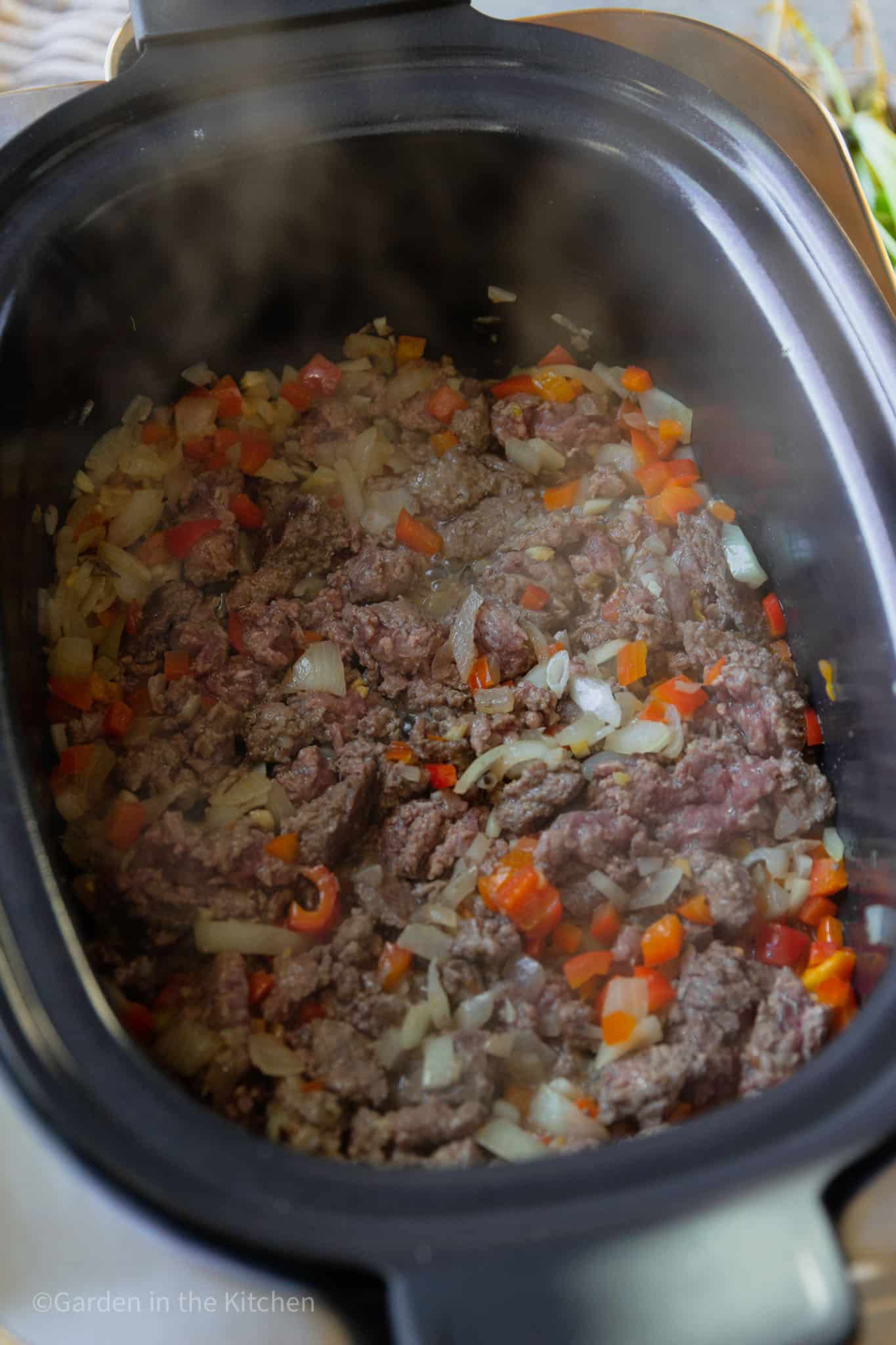 cooking raw ground meat, peppers, onions, and garlic in a slow cooker.