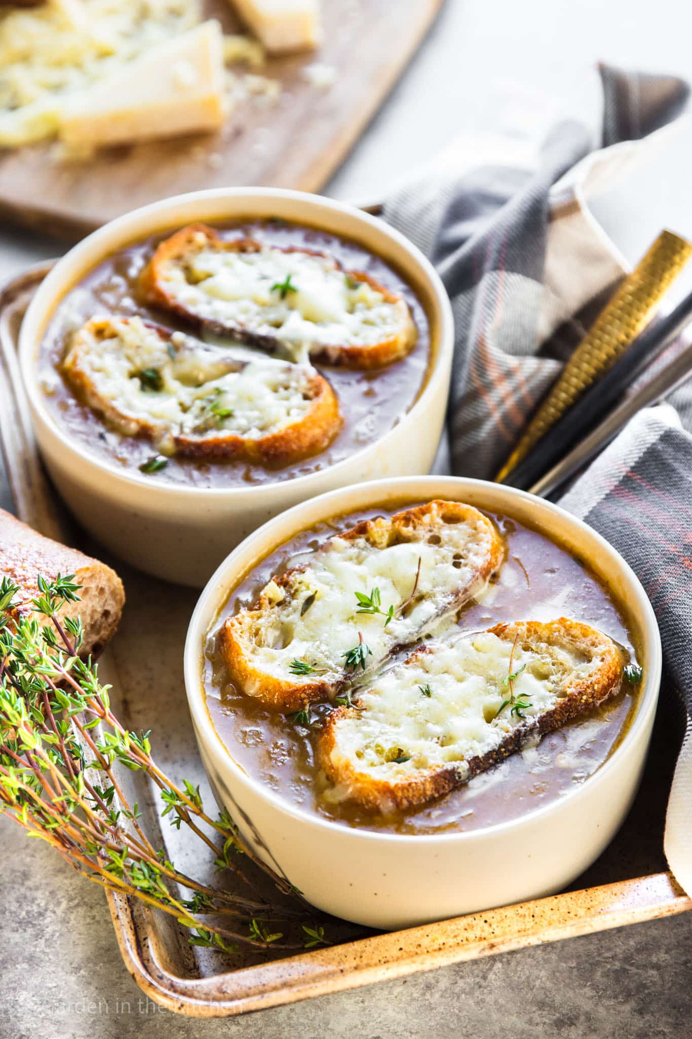 2 white bowls of french onion soup topped with toasted bread and melted cheese.