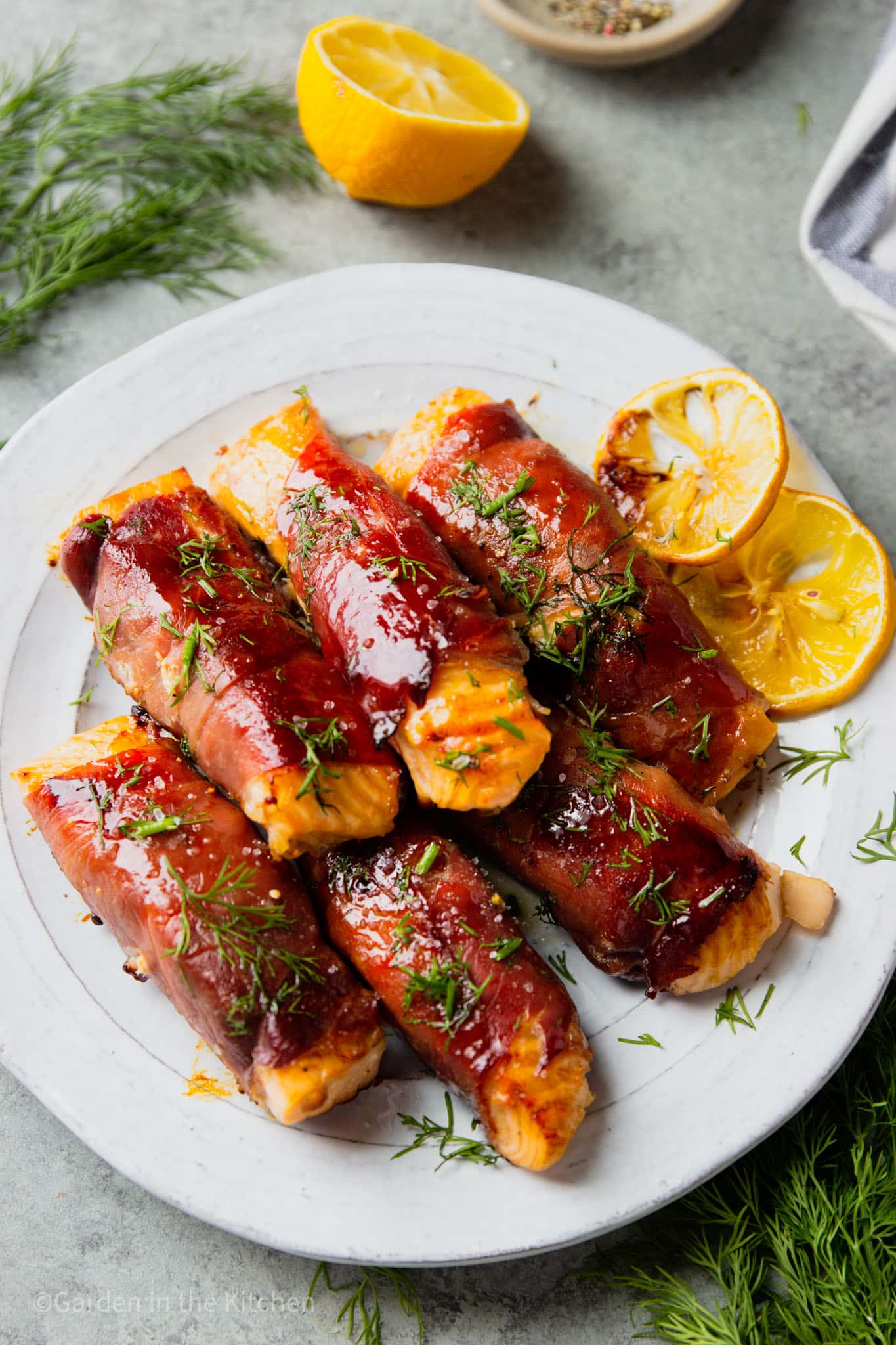 prosciutto wrapped salmon filets piled on top of each other on a white plate.