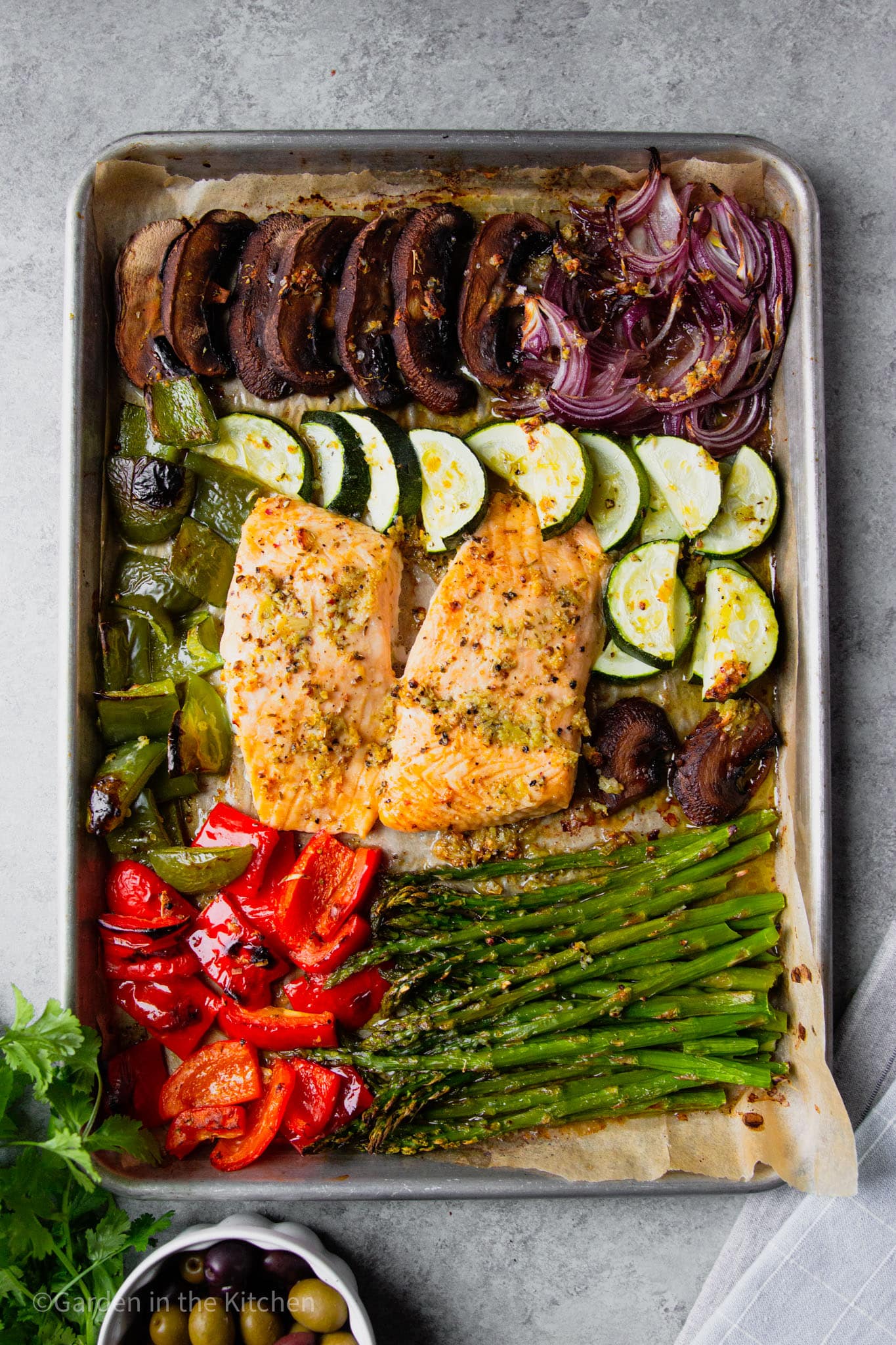 cooked salmon filets in the middle of a sheet pan filled with roasted vegetables.