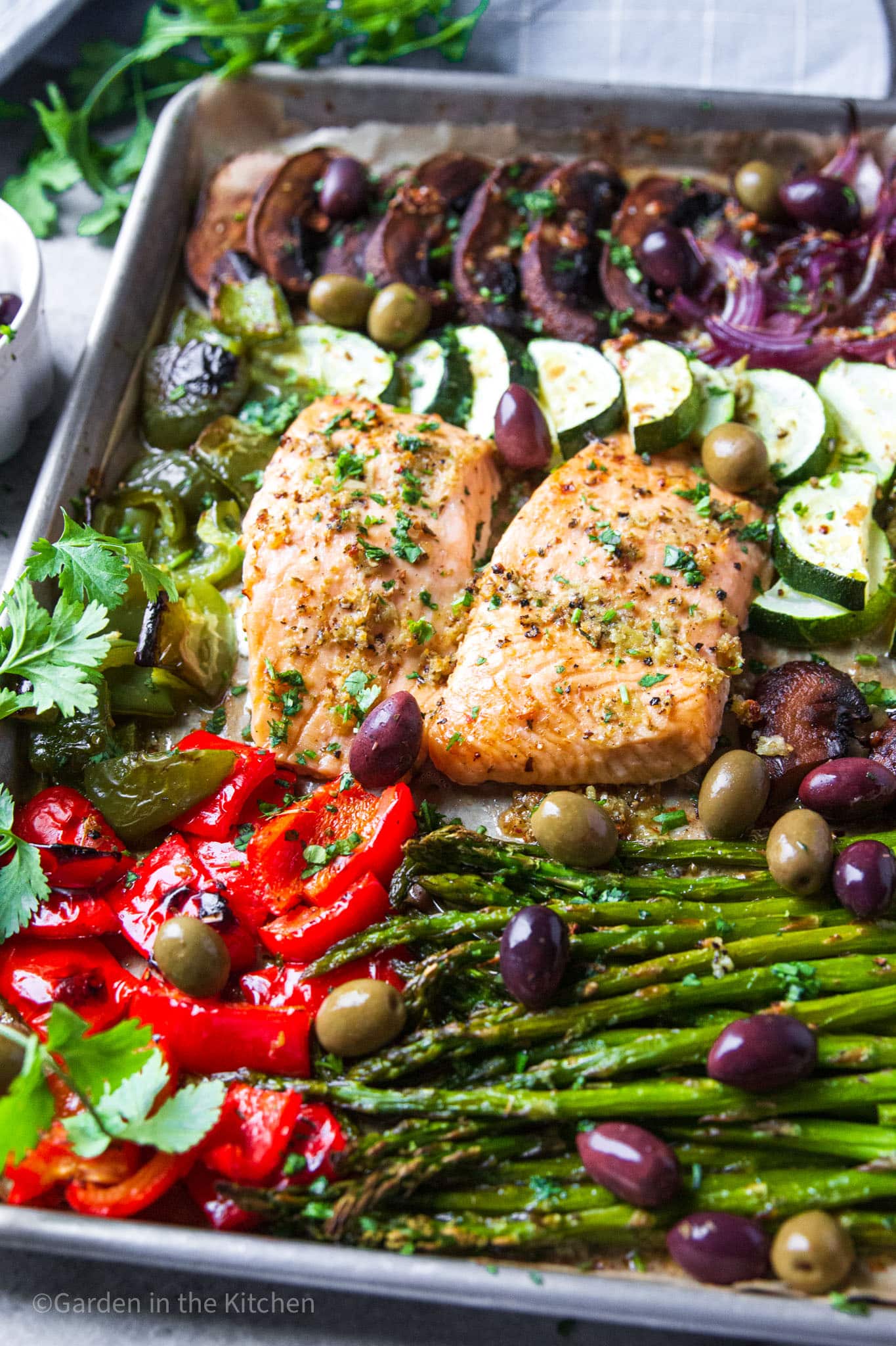 cooked salmon filets in the middle of a sheet pan filled with roasted vegetables.