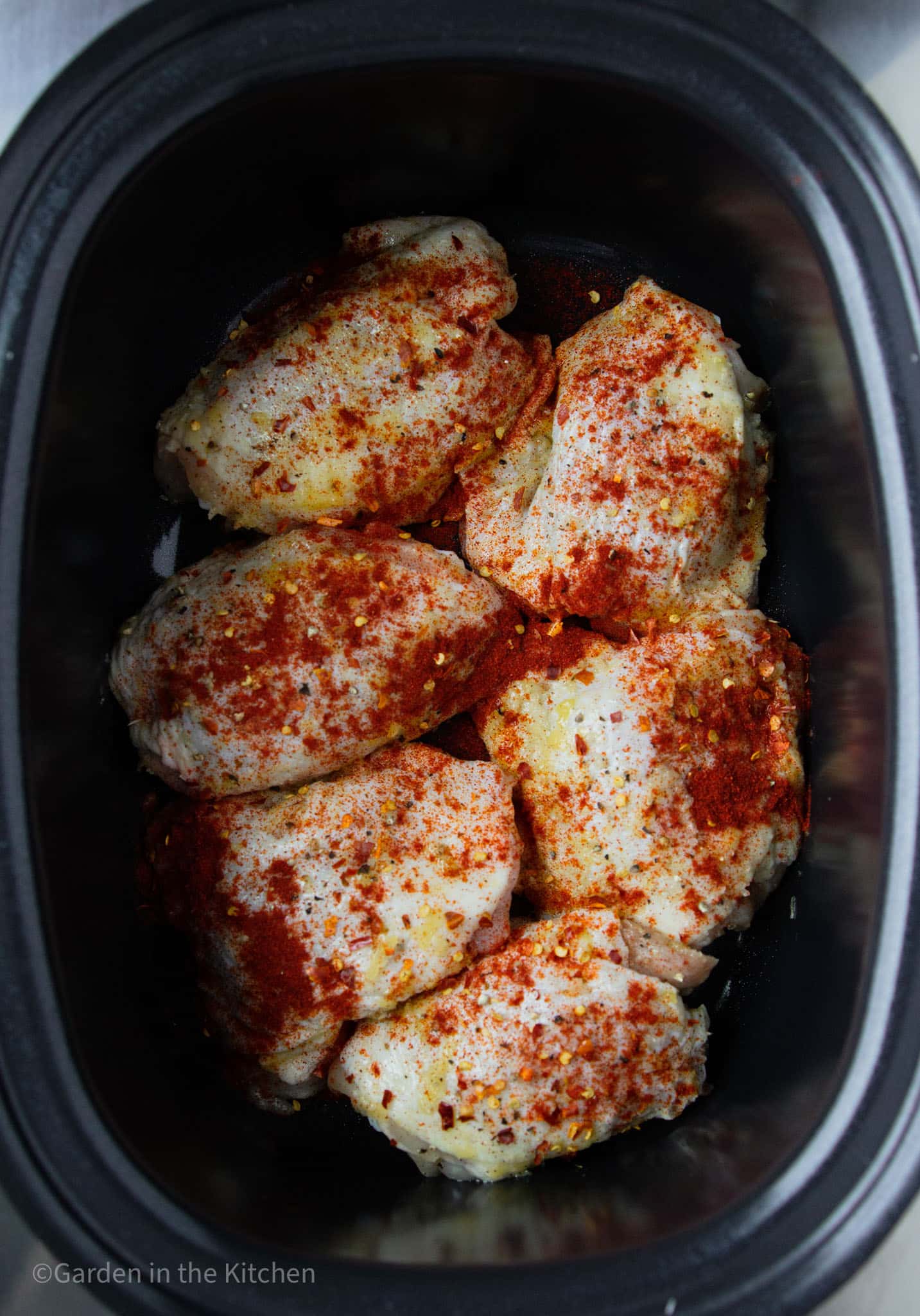 raw chicken thighs covered in paprika and chili flakes in a large slow cooker.