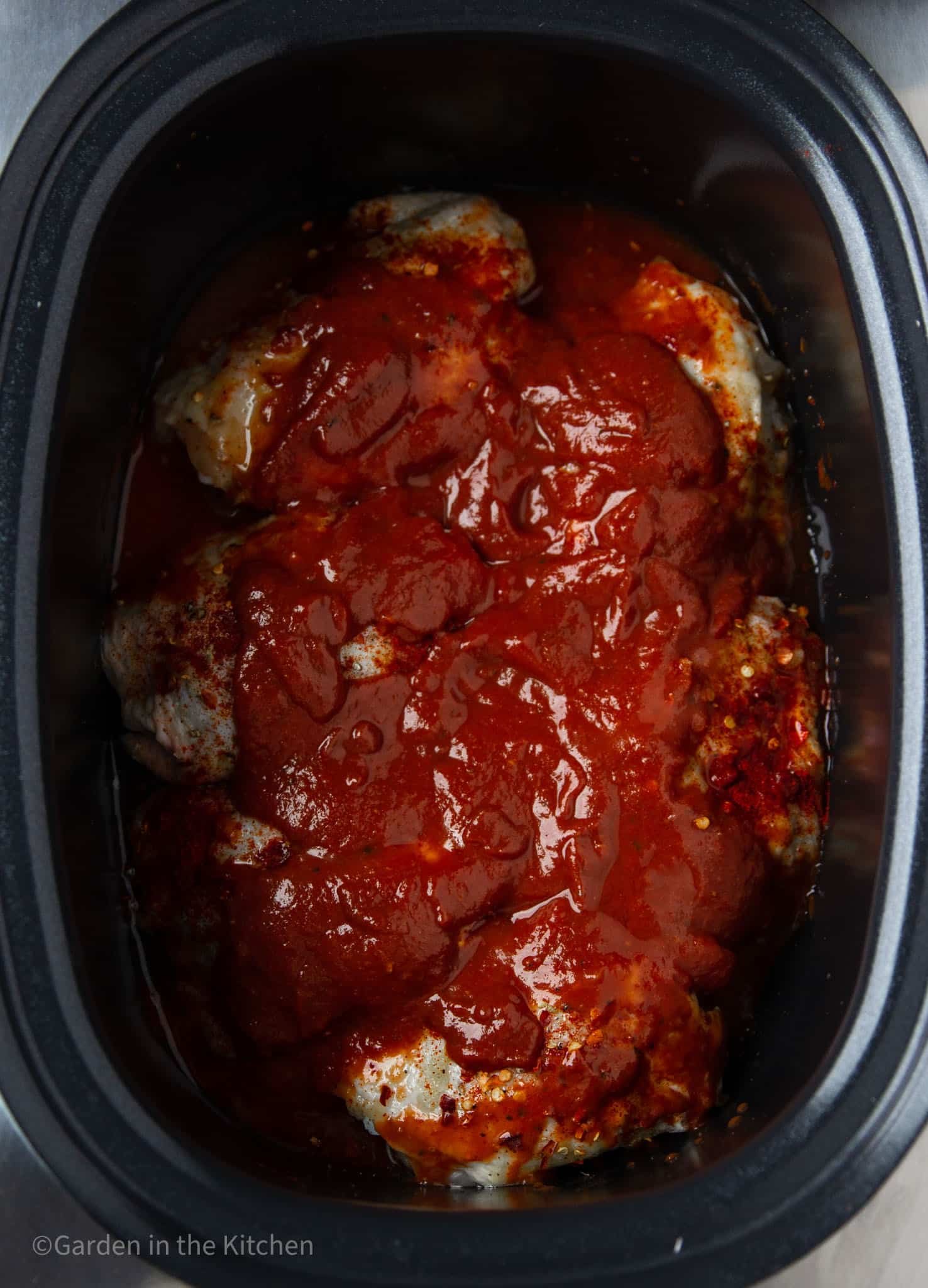 raw chicken thighs covered in bbq sauce in a large slow cooker.