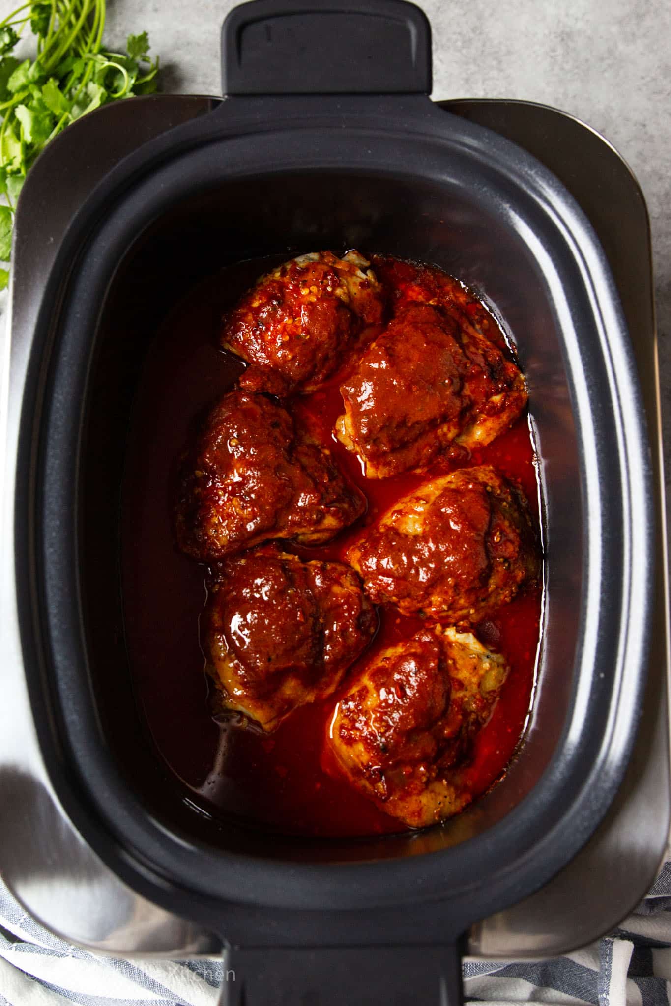 cooked chicken thighs covered in barbecue sauce in a large black slow cooker.