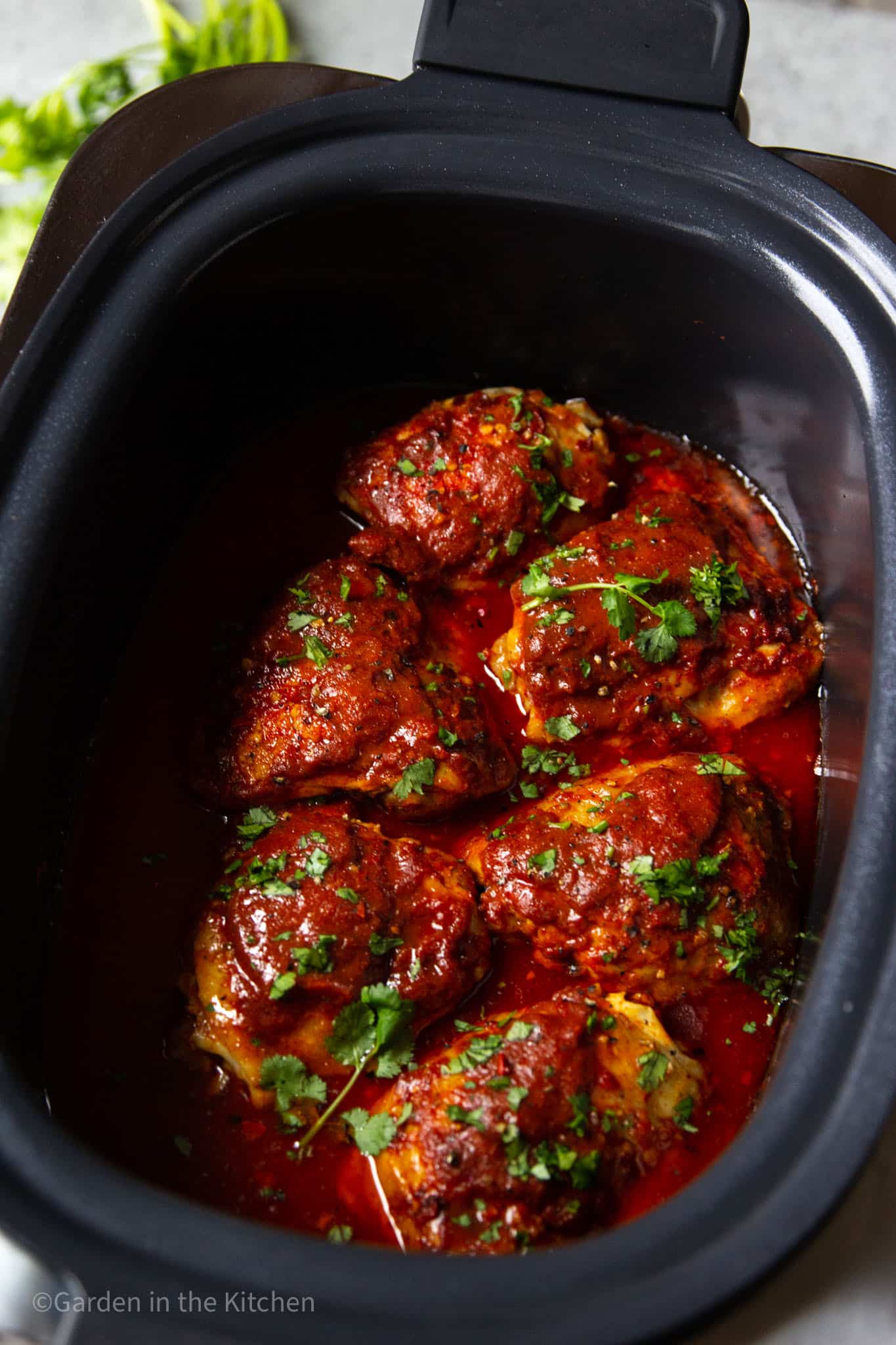 cooked bbq chicken thighs in a large black crockpot.