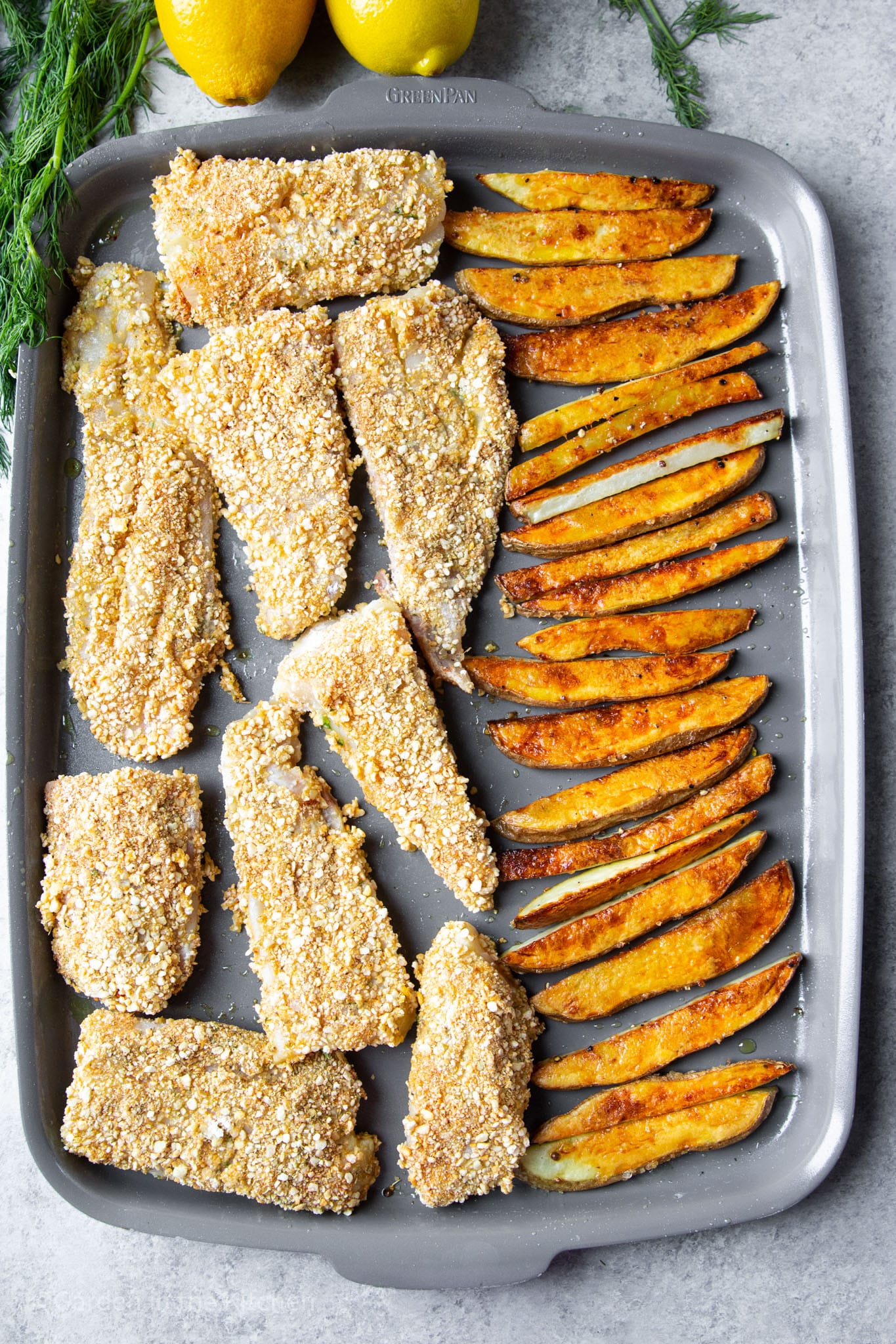 baked breaded fish filets and french fries on a metal baking sheet.