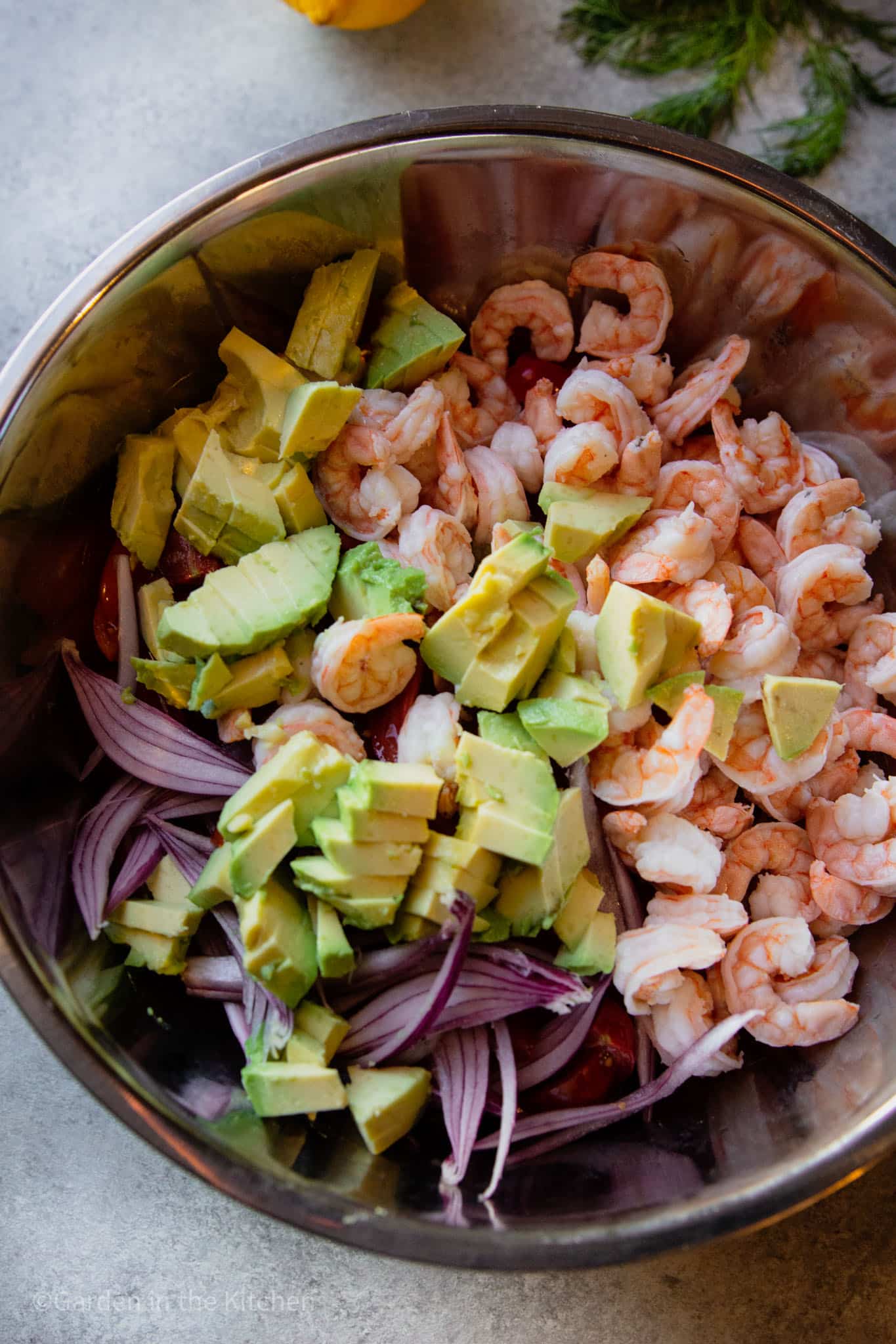 diced avocado, shrimp, chopped red onion, cucumbers, and tomatoes in a large metal bowl. 