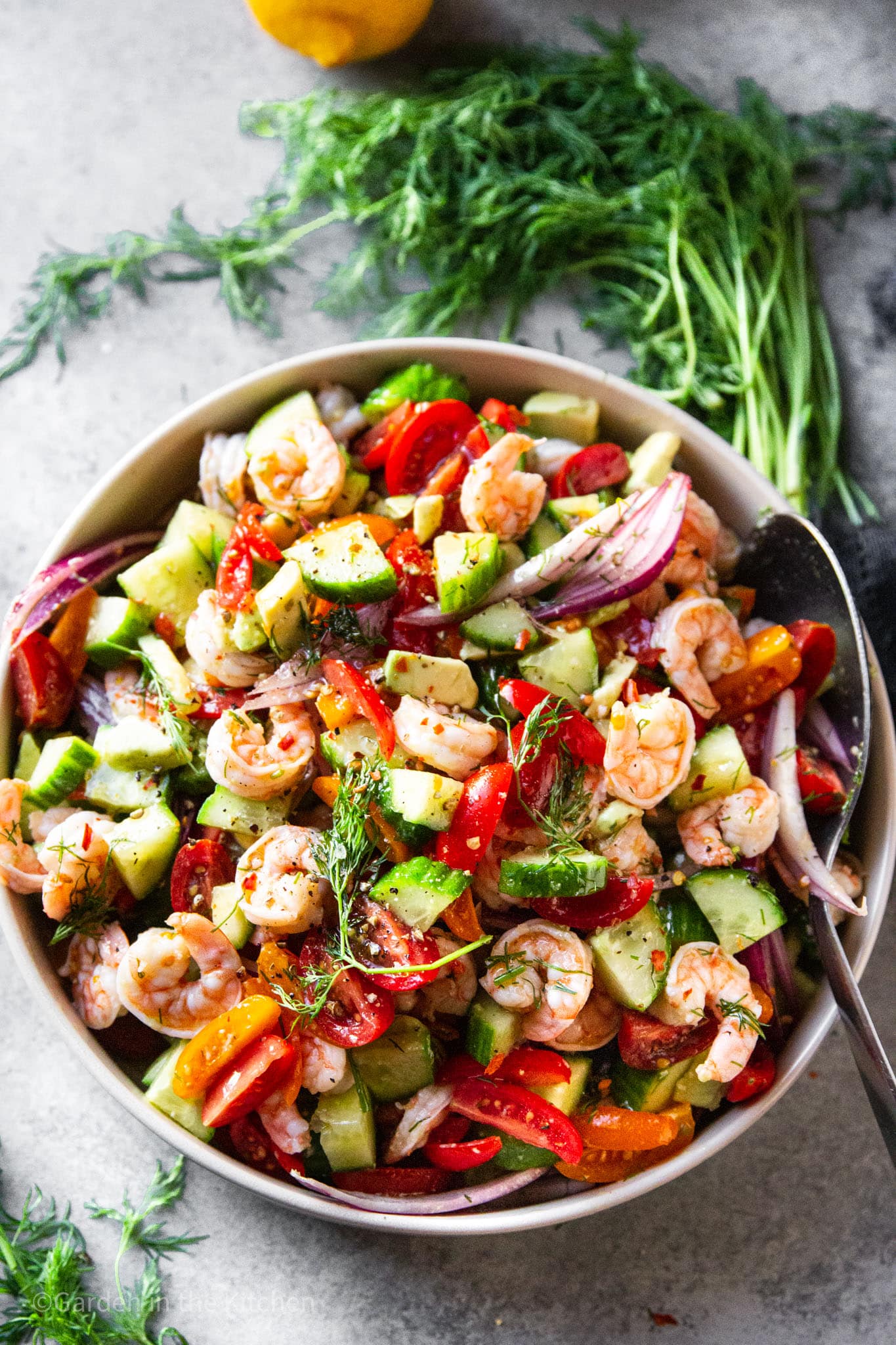 using a spoon to stir shrimp avocado salad in a large white bowl.