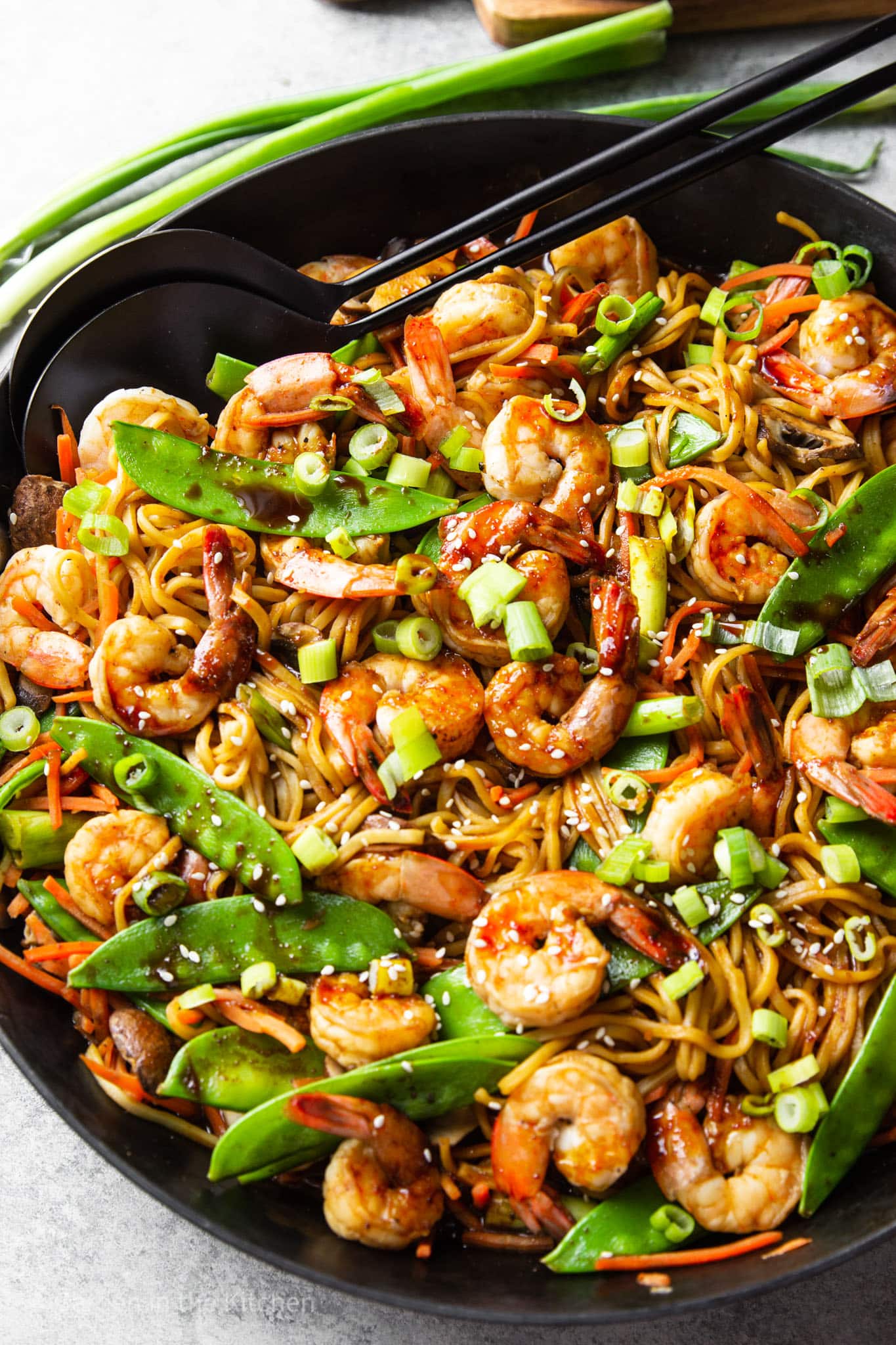 shrimp lo mein topped with scallions in a large black skillet.