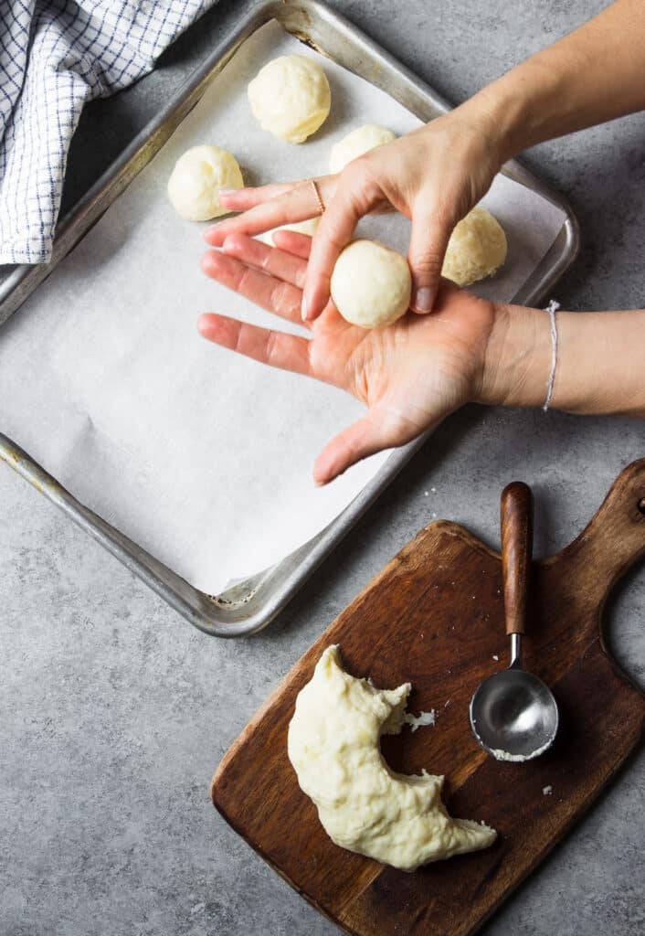 a hand holding a small ball of dough next to a larger ball of dough.