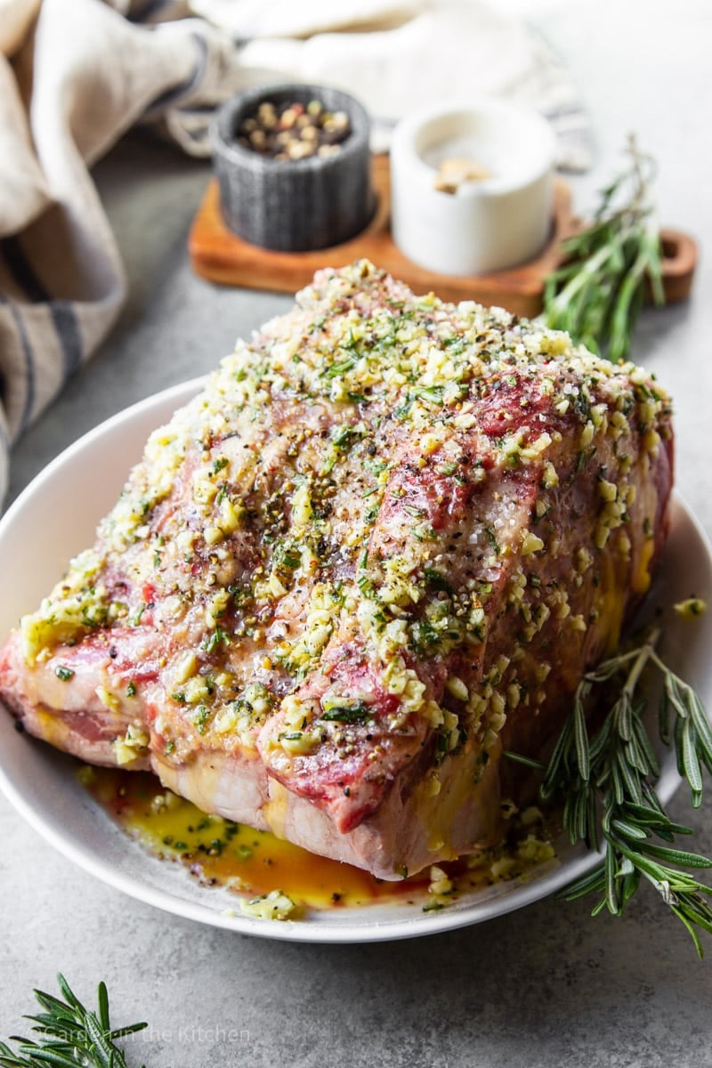 a raw garlic herb butter dressed prime rib roast in a white bowl.