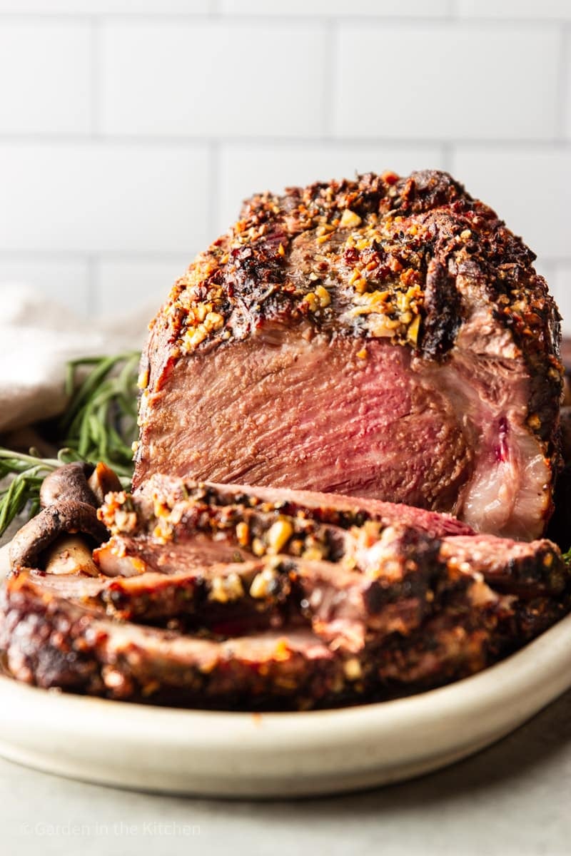 close up on a sliced prime rib roast on a white serving plate.