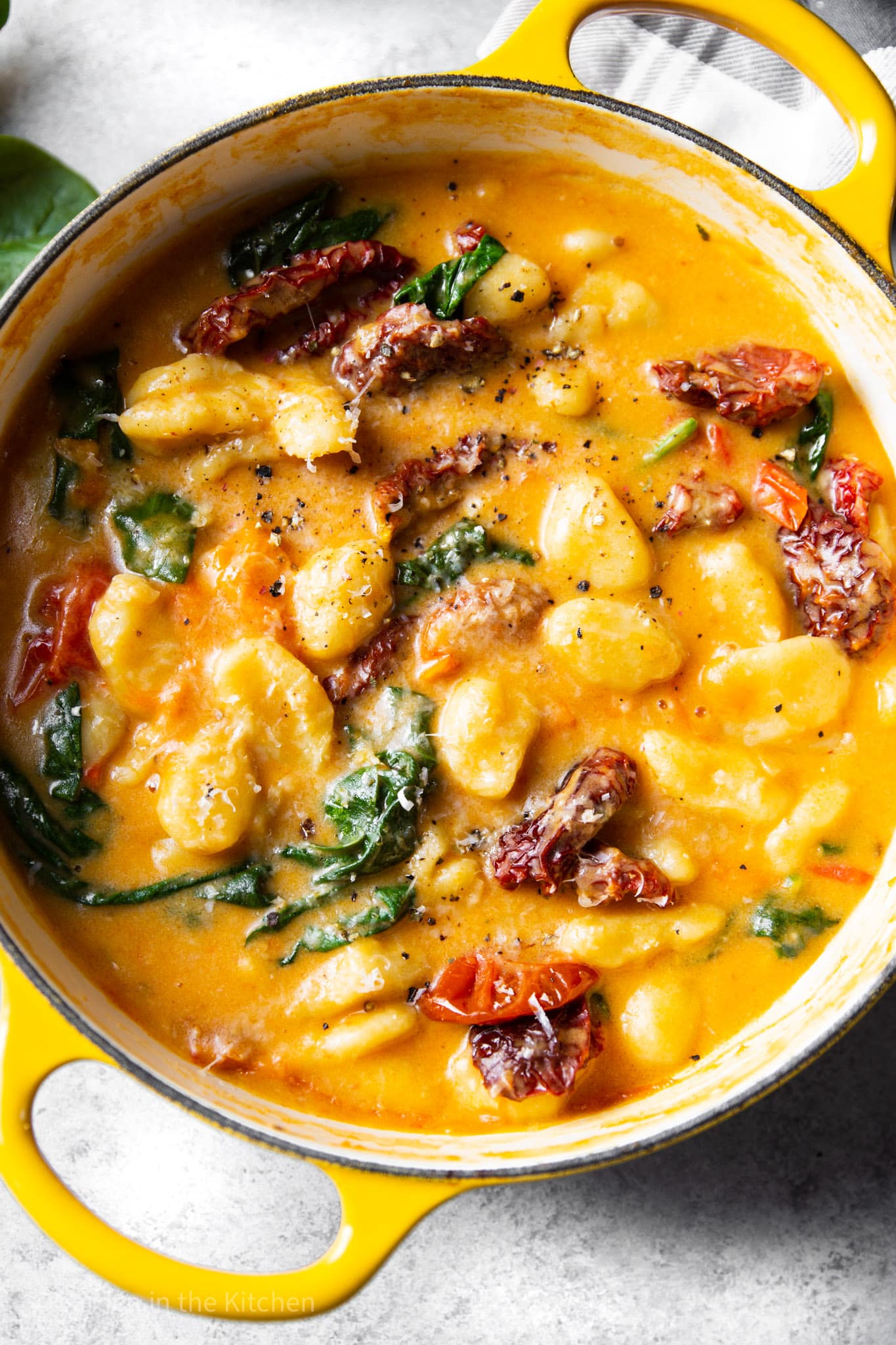 a yellow pot filled with cooked tomatoes, spinach, gnocchi, and cream sauce.