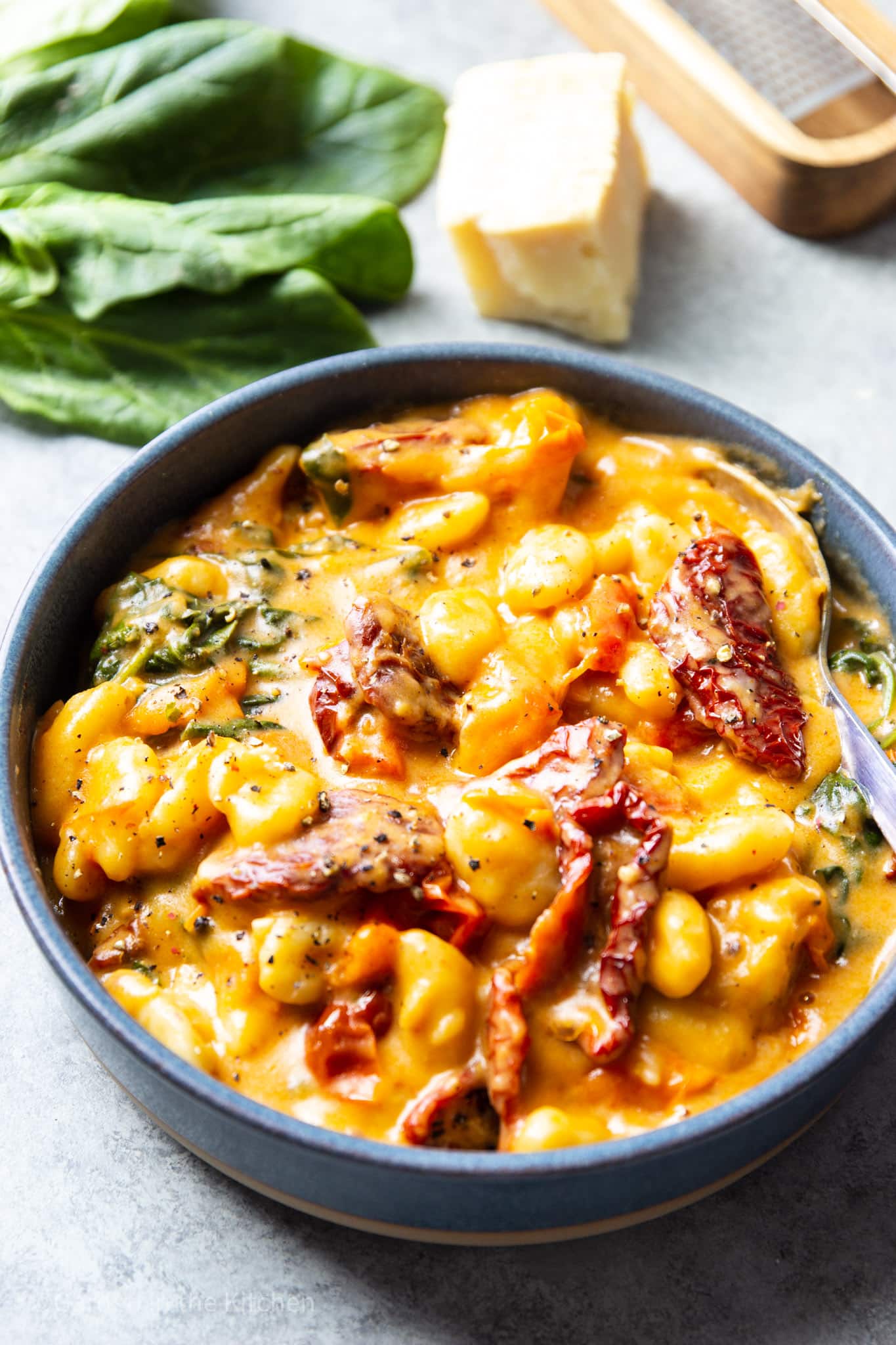 close up on sun dried tomatoes and gnocchi in a cheesy, creamy sauce in a gray bowl.