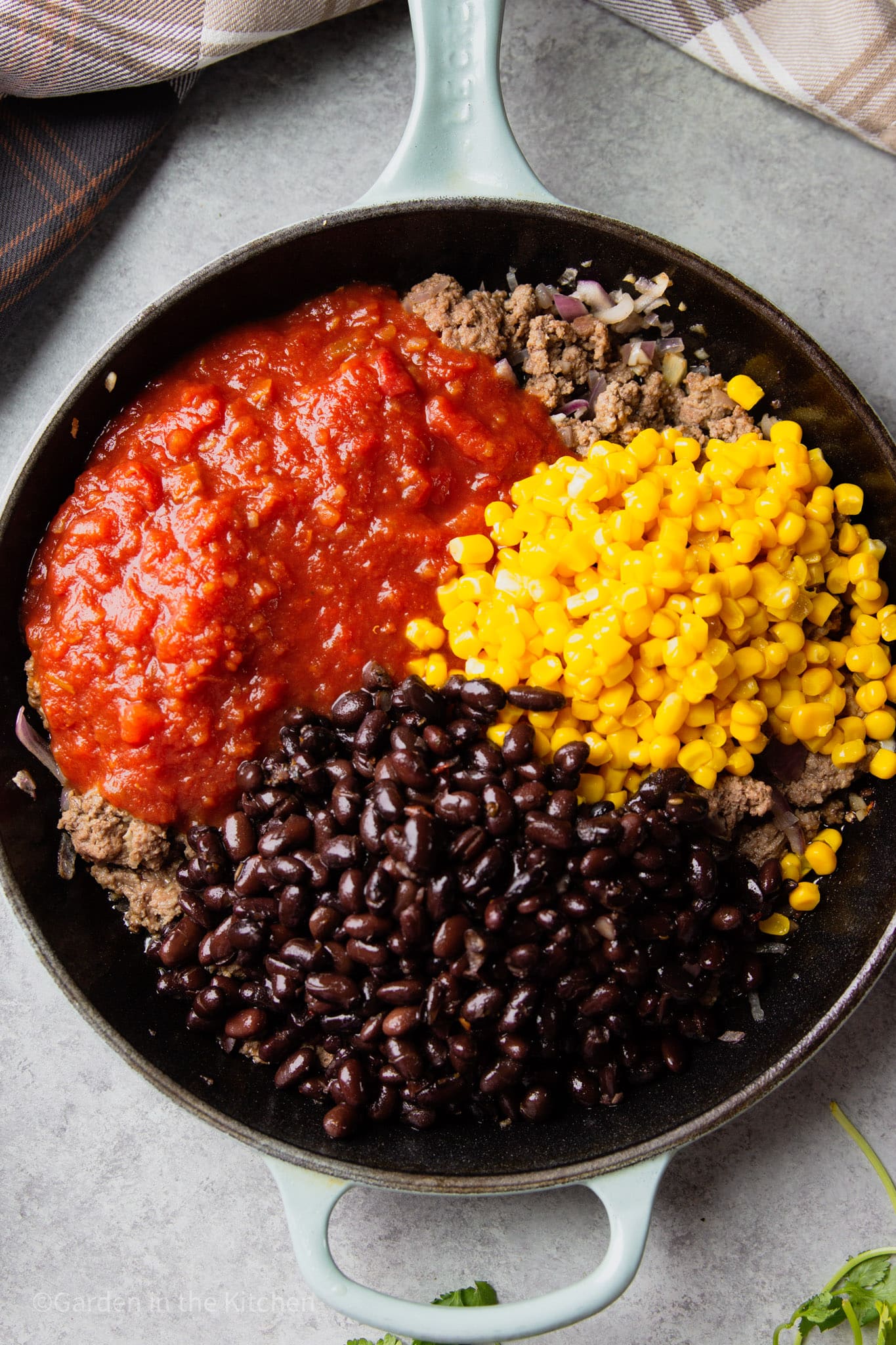 corn, black beans, and red salsa on top of cooked ground beef in a black skillet.