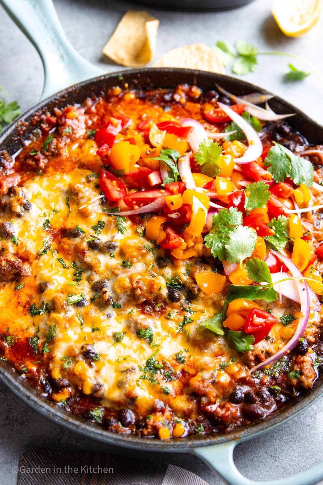 ground beef taco dip in a black skillet topped with tomato salsa.