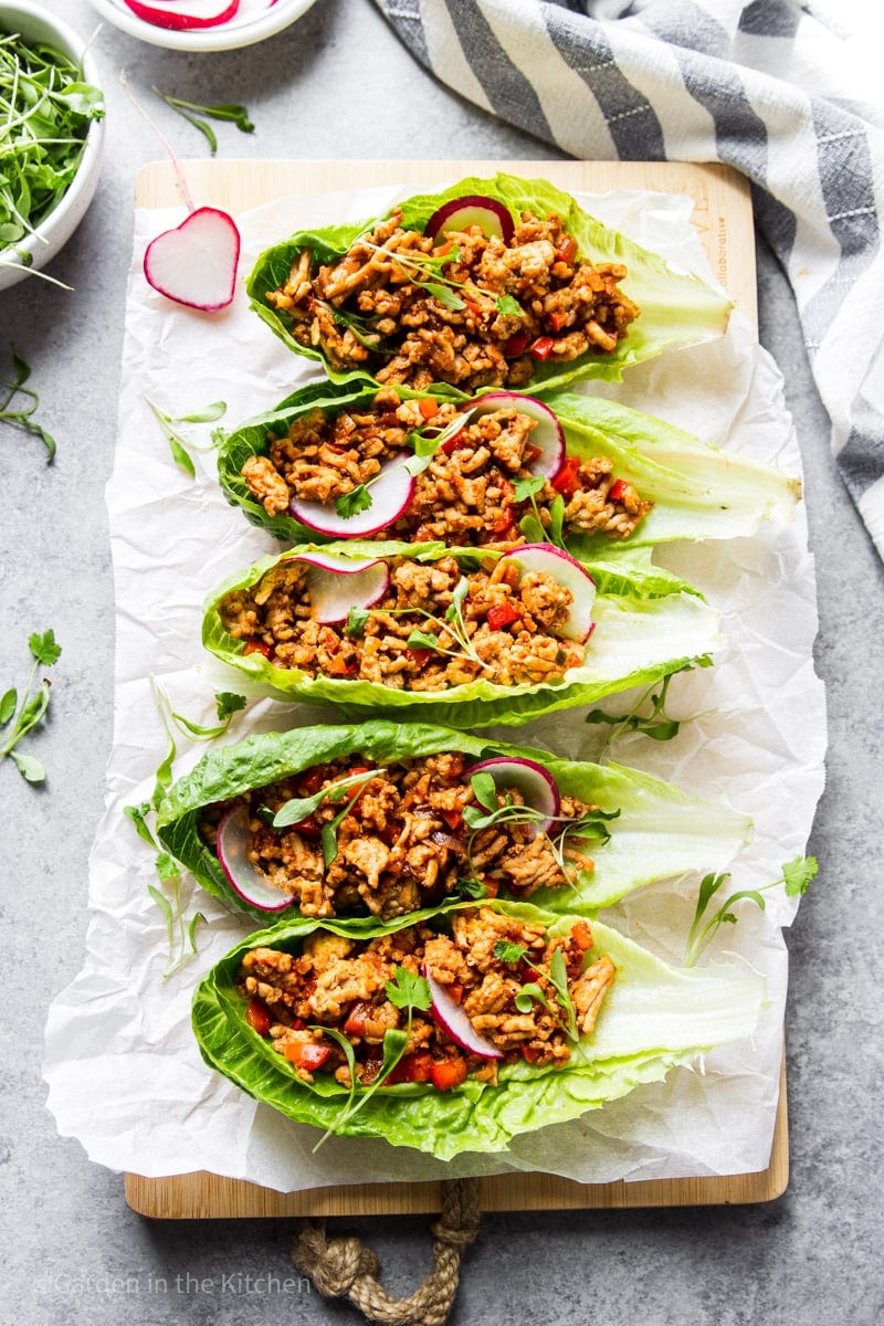 a row of ground chicken-stuffed lettuce wraps topped with microgreens and sliced radishes.