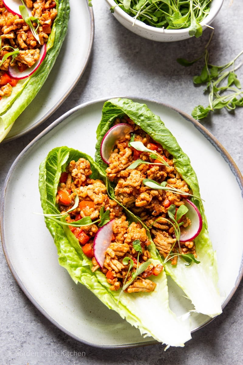 2 ground chicken-stuffed lettuce wraps on a white plate.